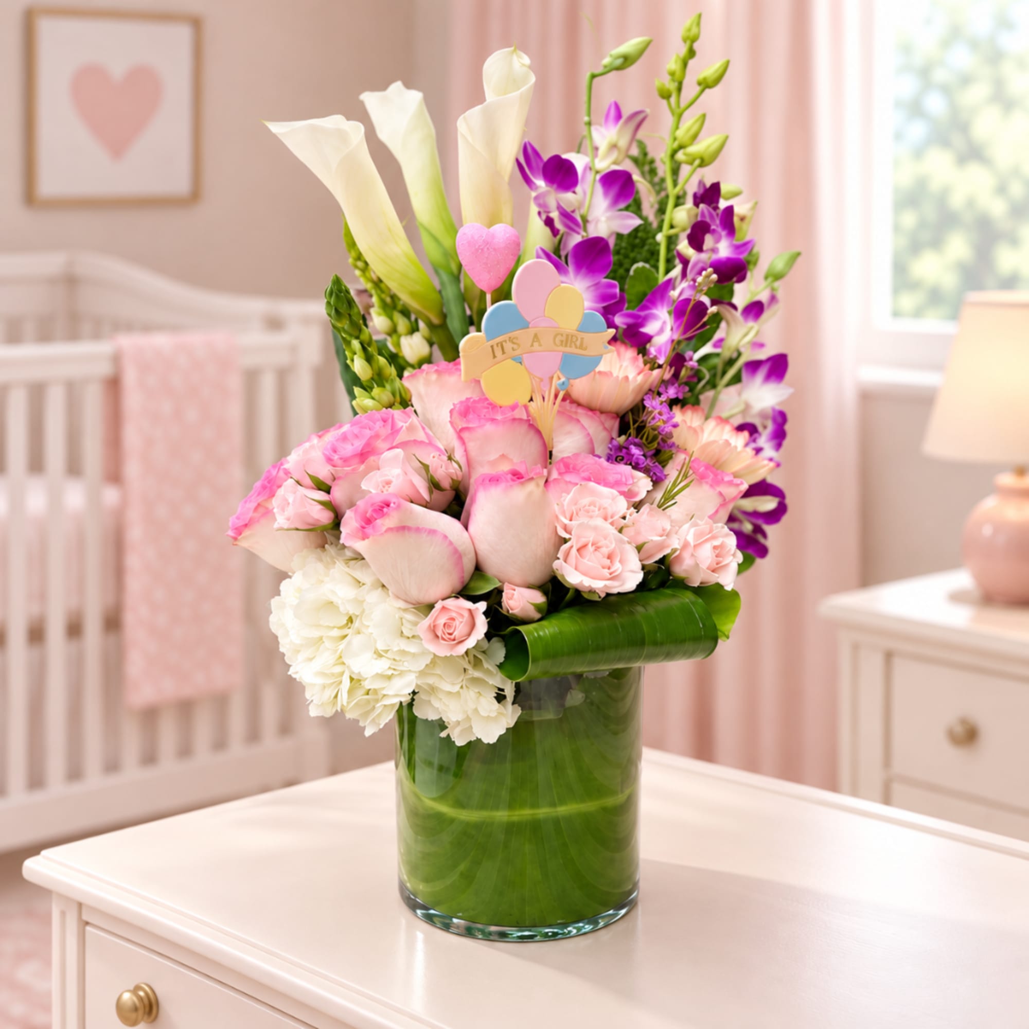 Pink and white floral arrangement in a glass vase with an "It's a Girl" topper