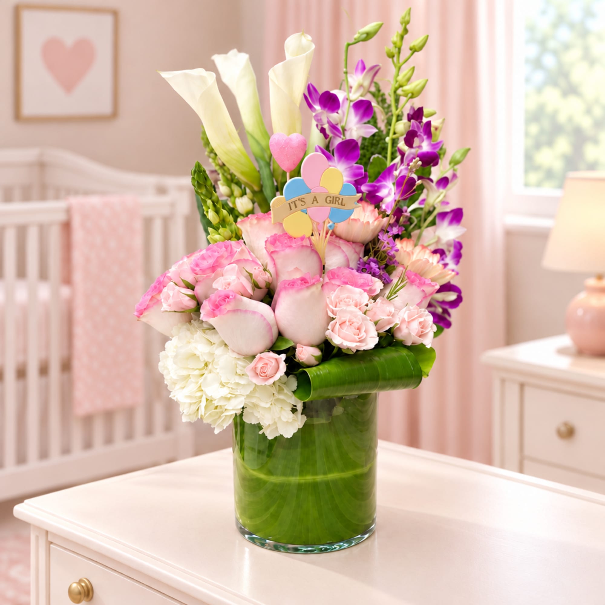 Pink and white floral arrangement in a glass vase with an "It's a Girl" pick
