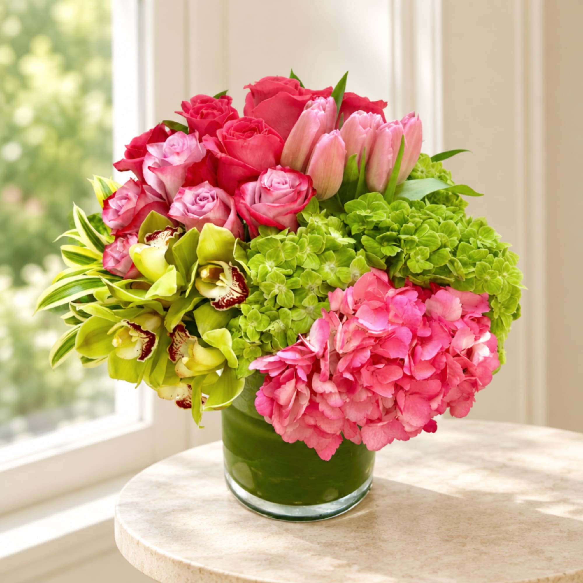 Pink roses, tulips, orchids, and hydrangeas in a glass vase