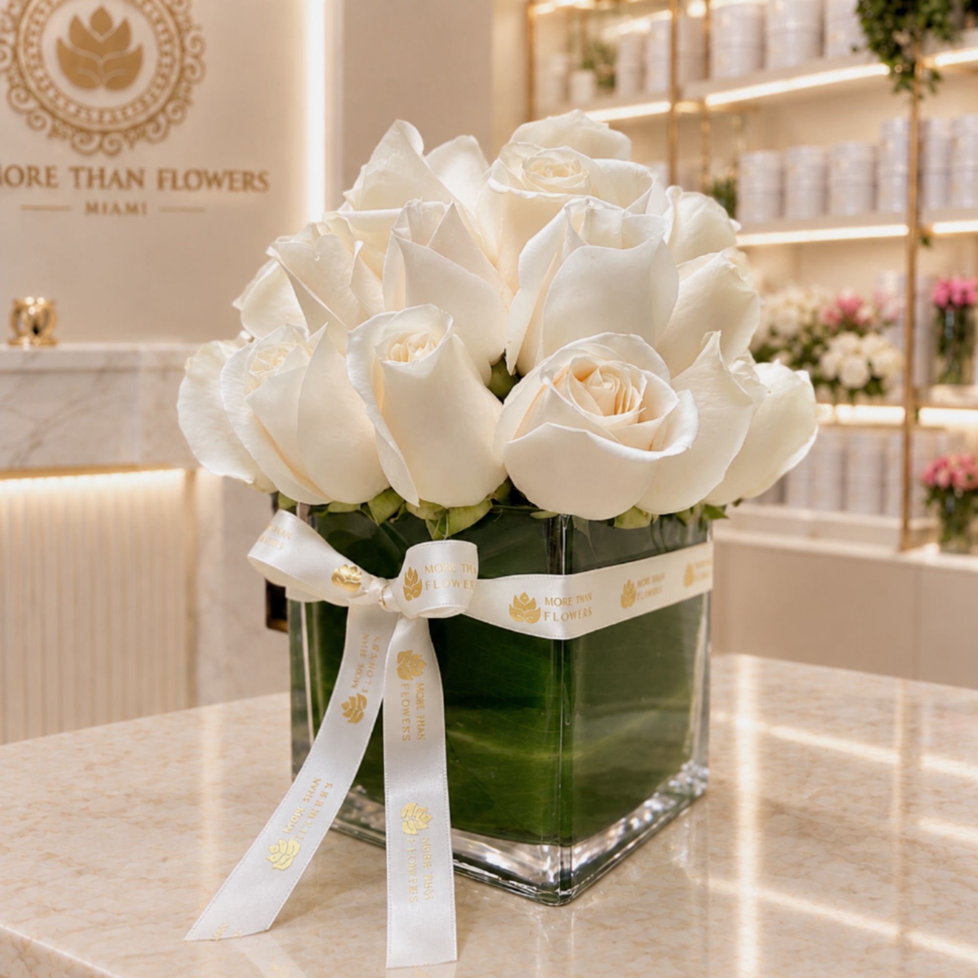 White roses arranged in a square glass vase with a ribbon bow