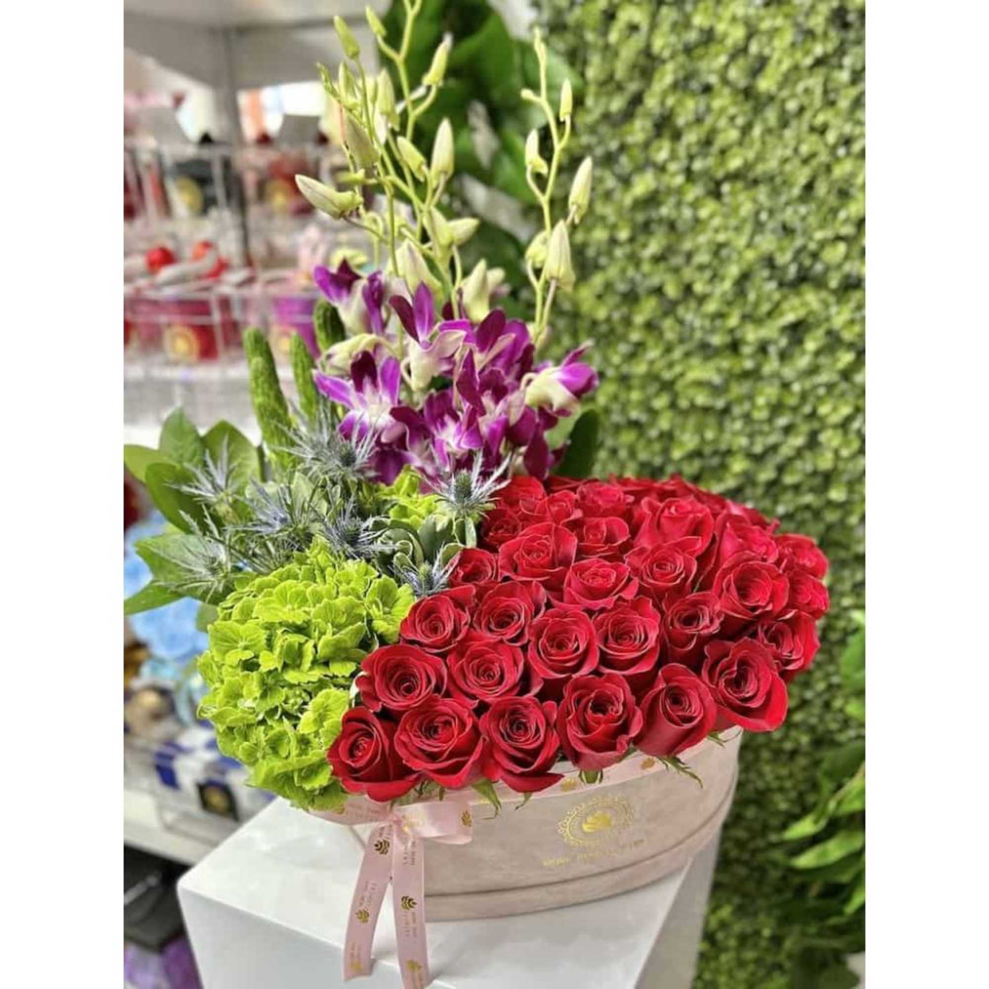 Oval box arrangement with red roses, green hydrangea, purple orchids, and blue thistles