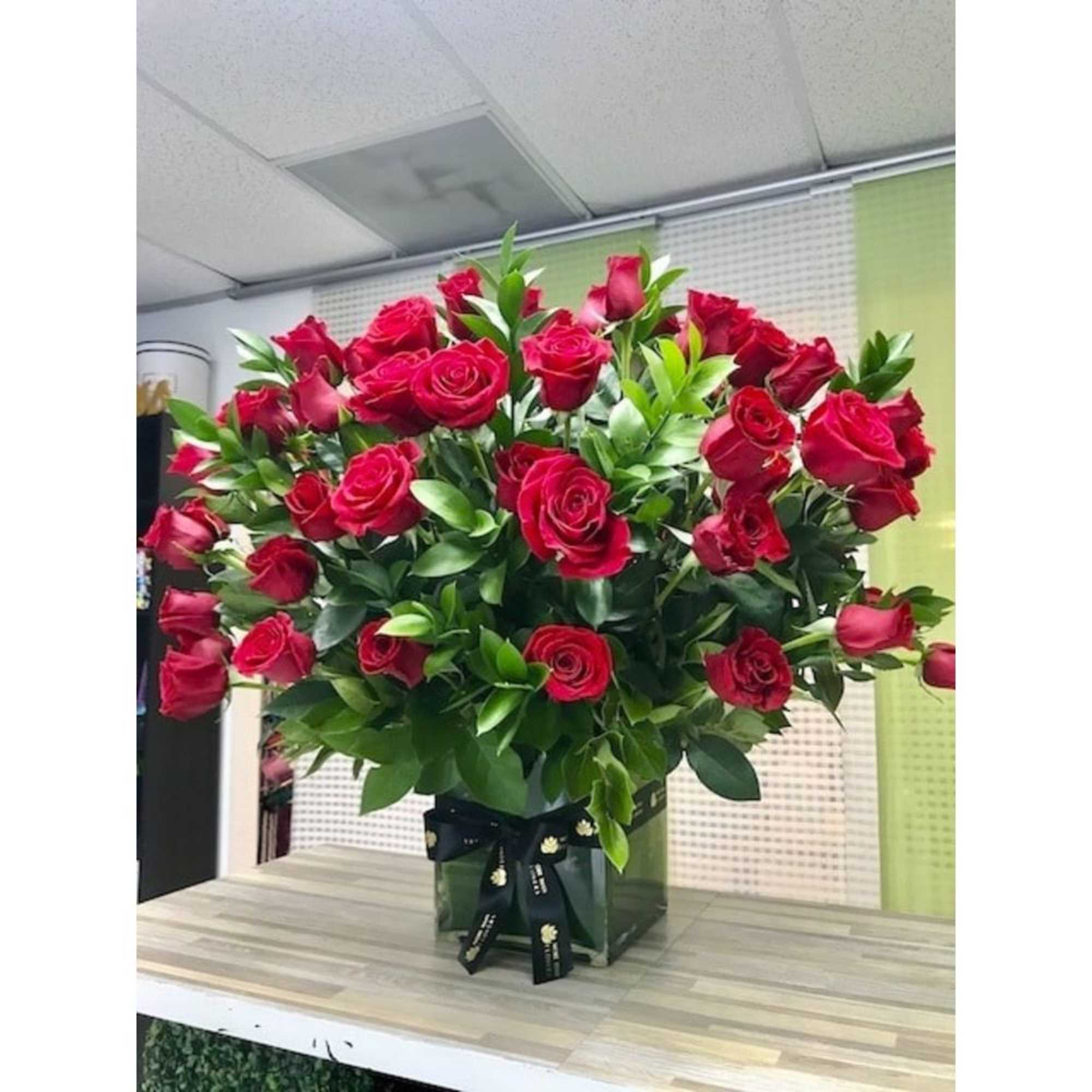 Large arrangement of red roses in a square glass vase with black ribbon