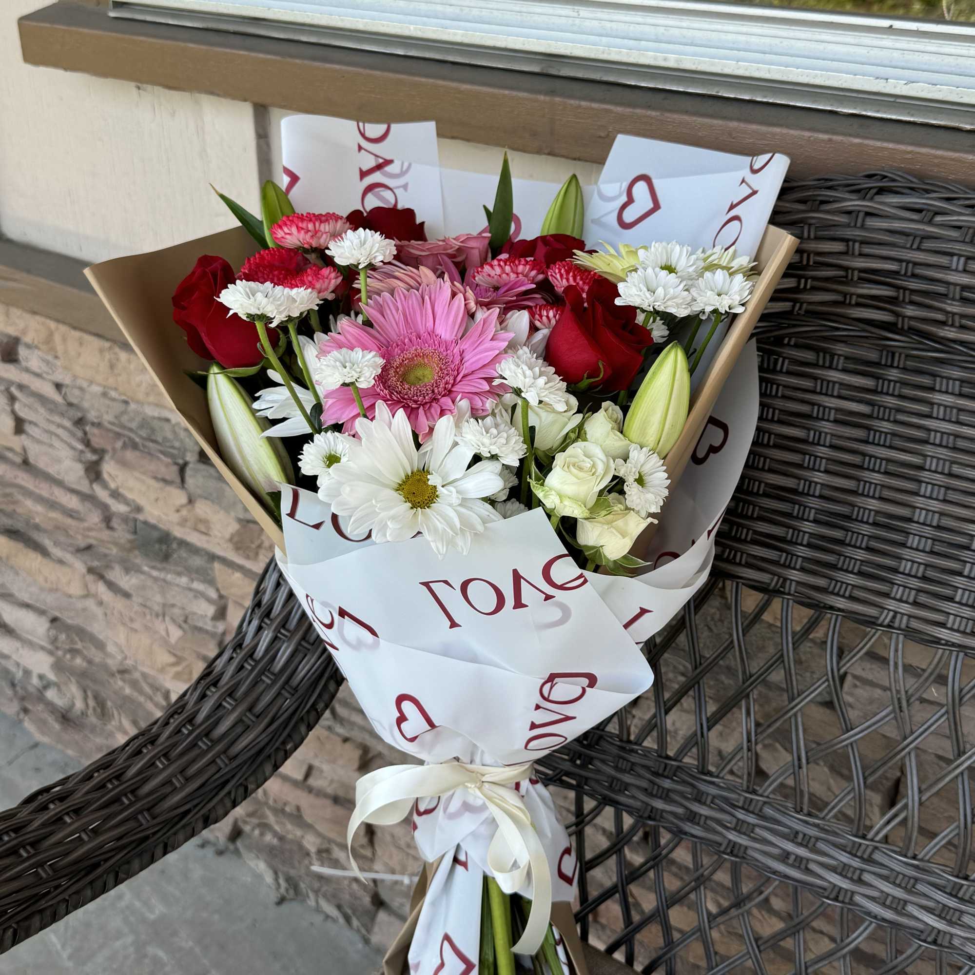 Bouquet of pink, red, and white flowers wrapped in paper with a ribbon