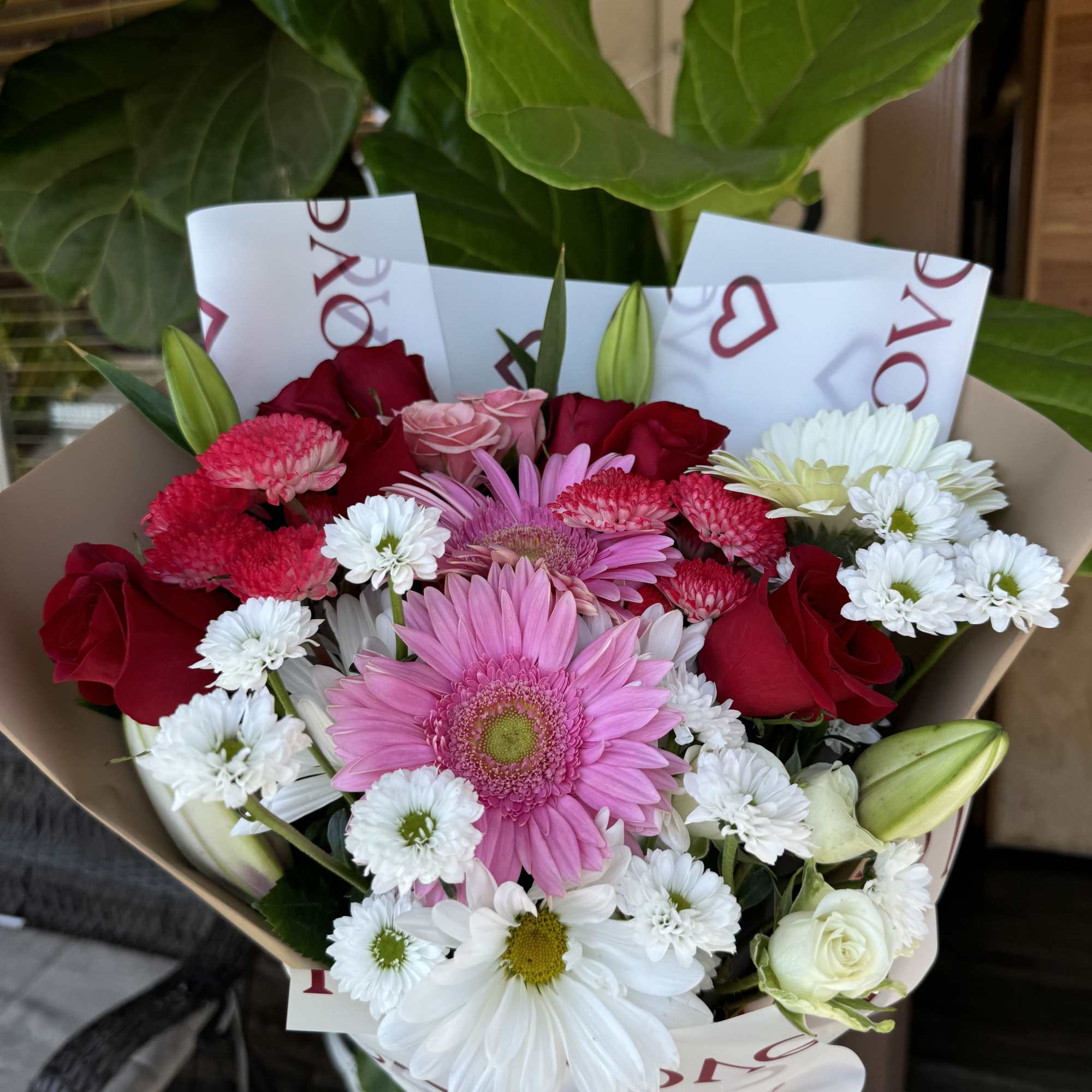 Bouquet of pink gerbera daisies, red roses, and white daisies wrapped in paper
