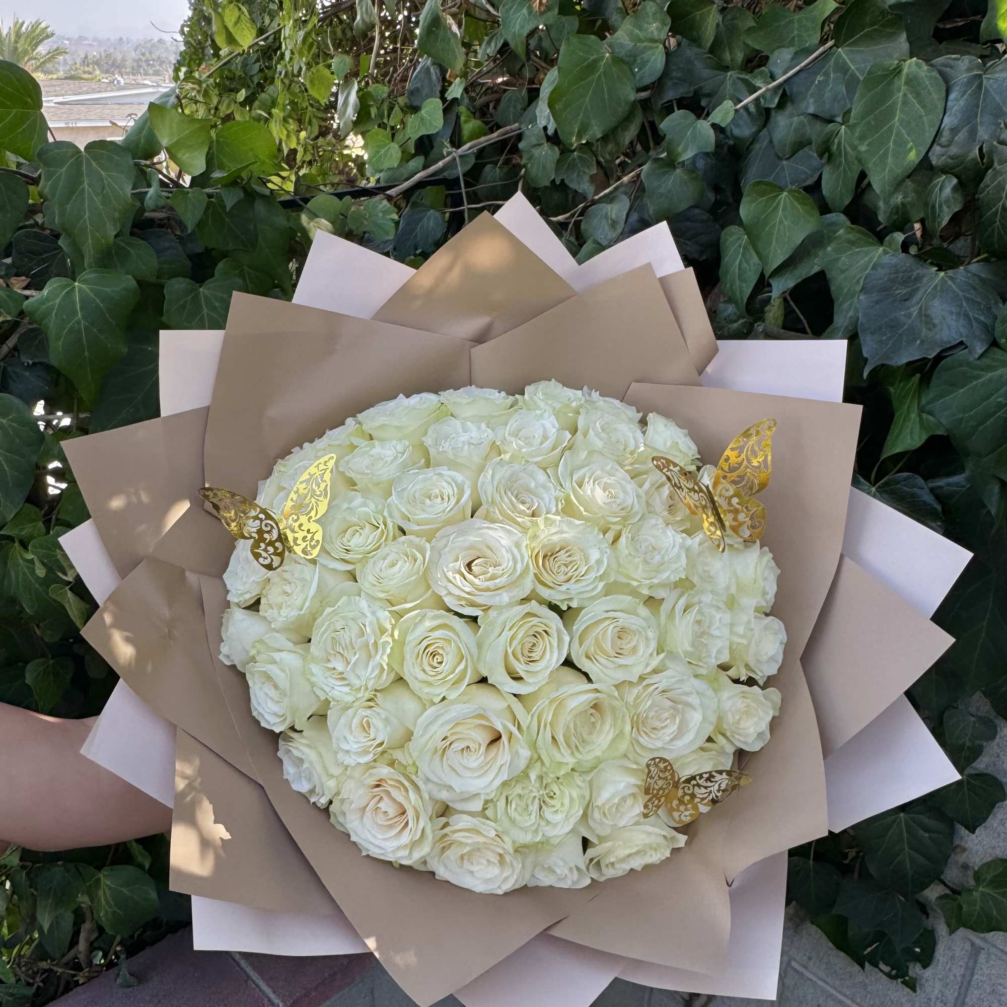 Bouquet of white roses wrapped in tan paper with gold butterfly accents