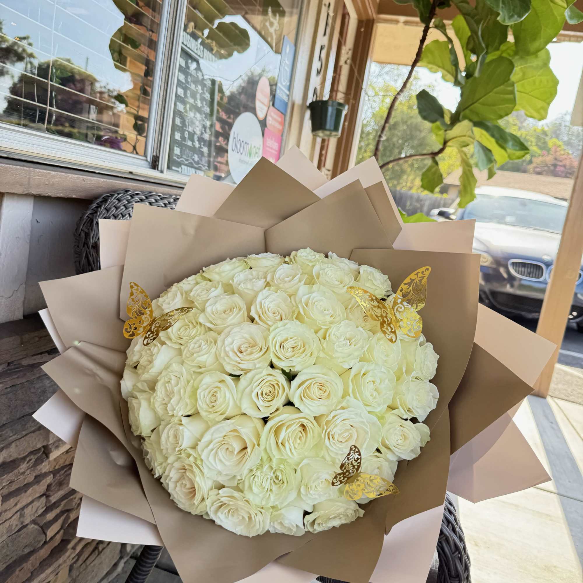 Large bouquet of cream roses wrapped in tan paper with gold butterfly accents