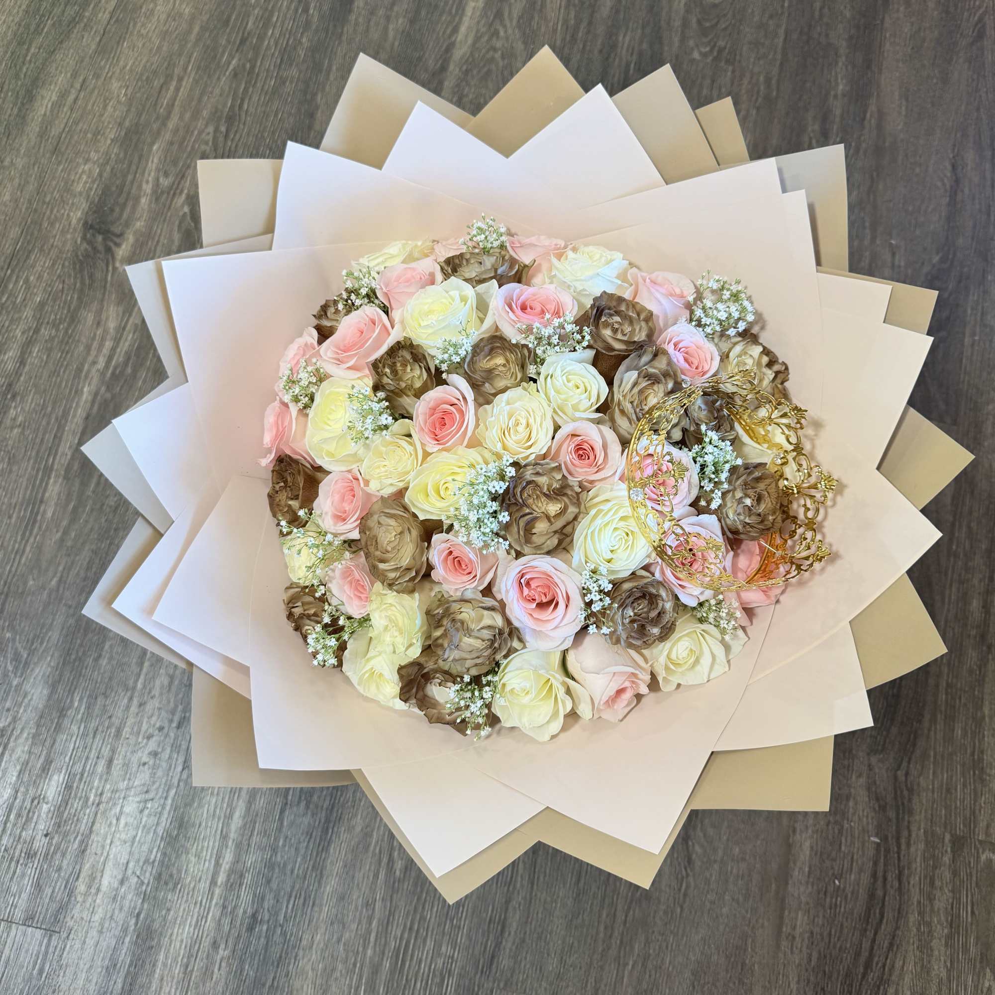 Round bouquet of pink, cream, and brown roses wrapped in layered paper