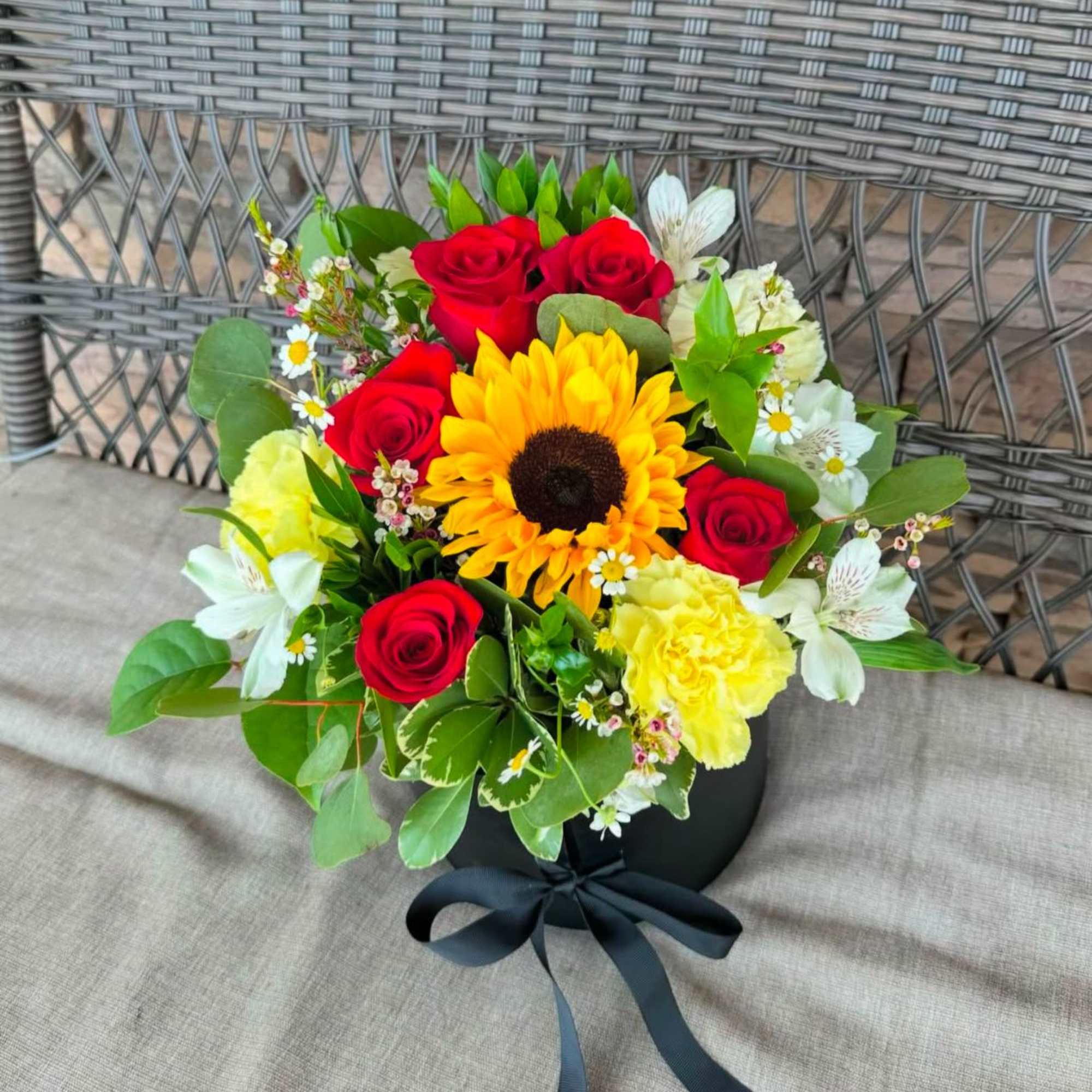 Bouquet of red roses, a sunflower, and yellow carnations in a black box