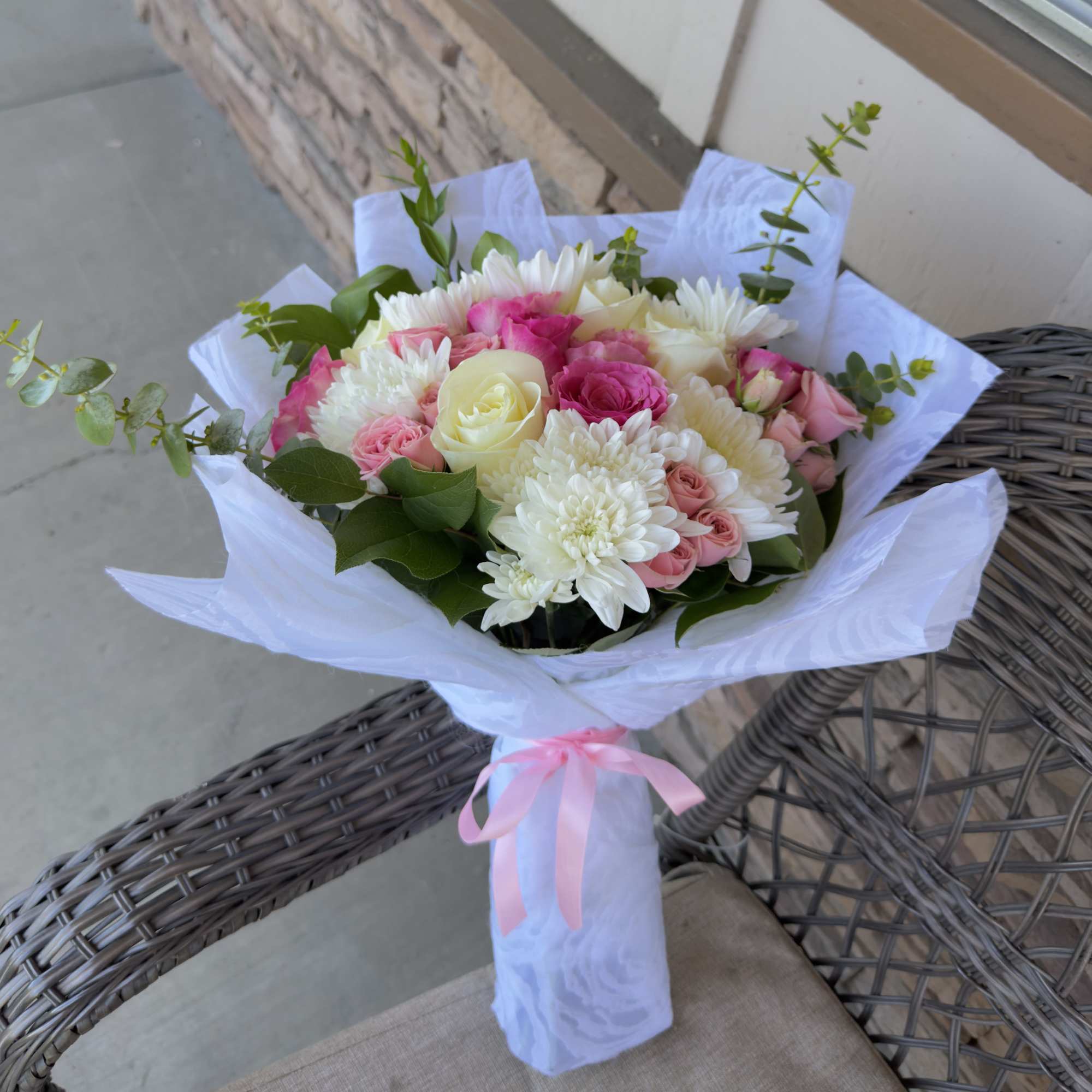 Bouquet of pink and white flowers wrapped in white paper with a pink ribbon