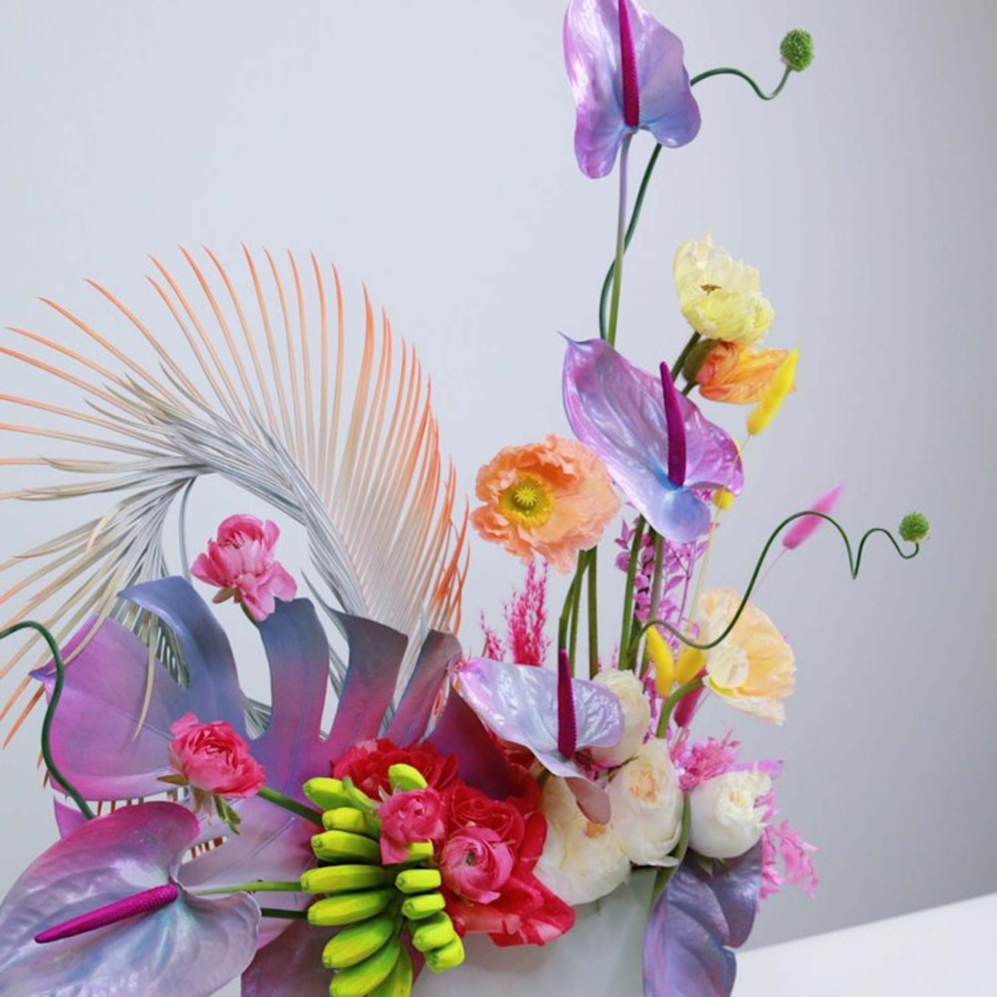 Colorful floral arrangement in a white rectangular vase with purple anthuriums