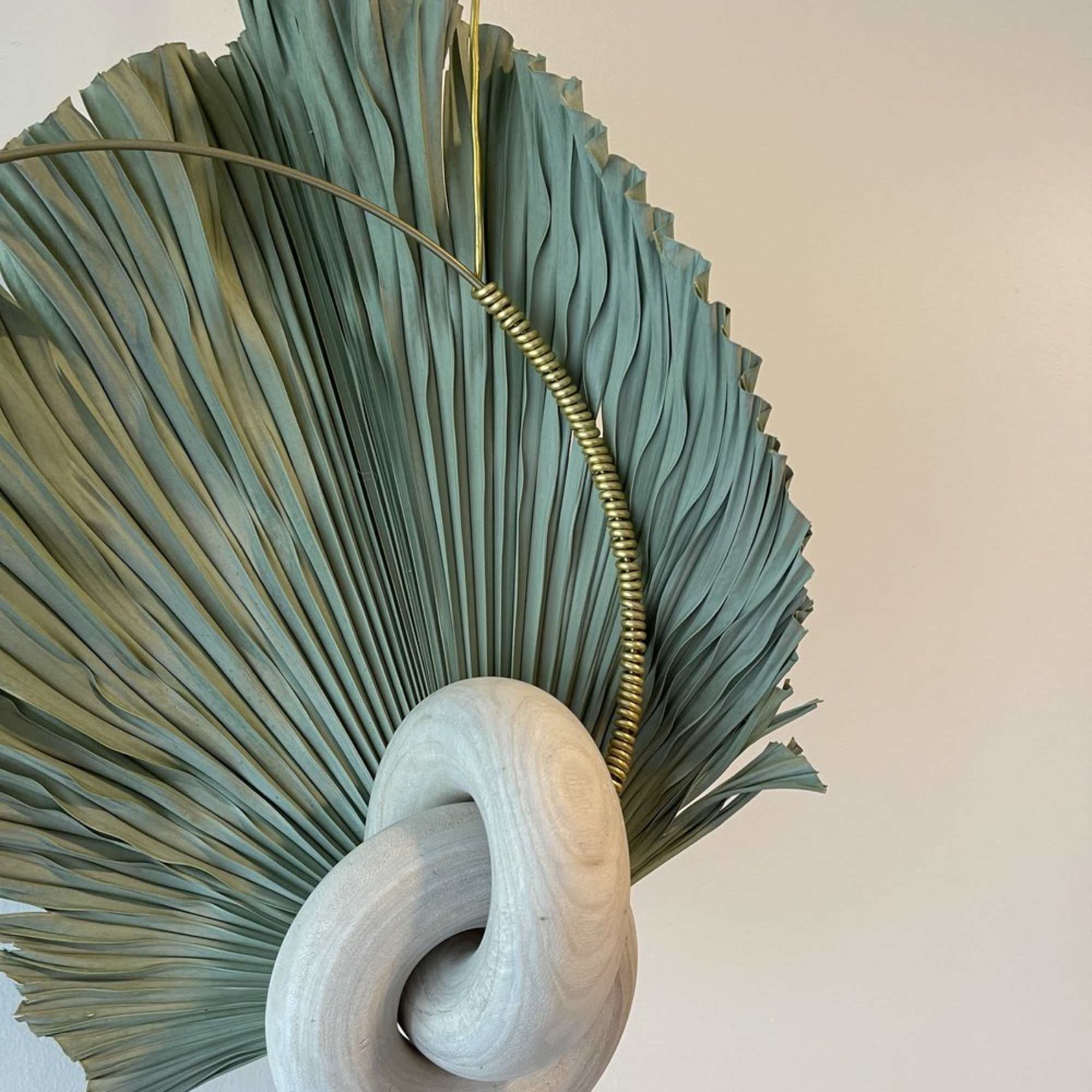 Abstract wall sculpture with folded teal fan shapes and a pale wooden loop