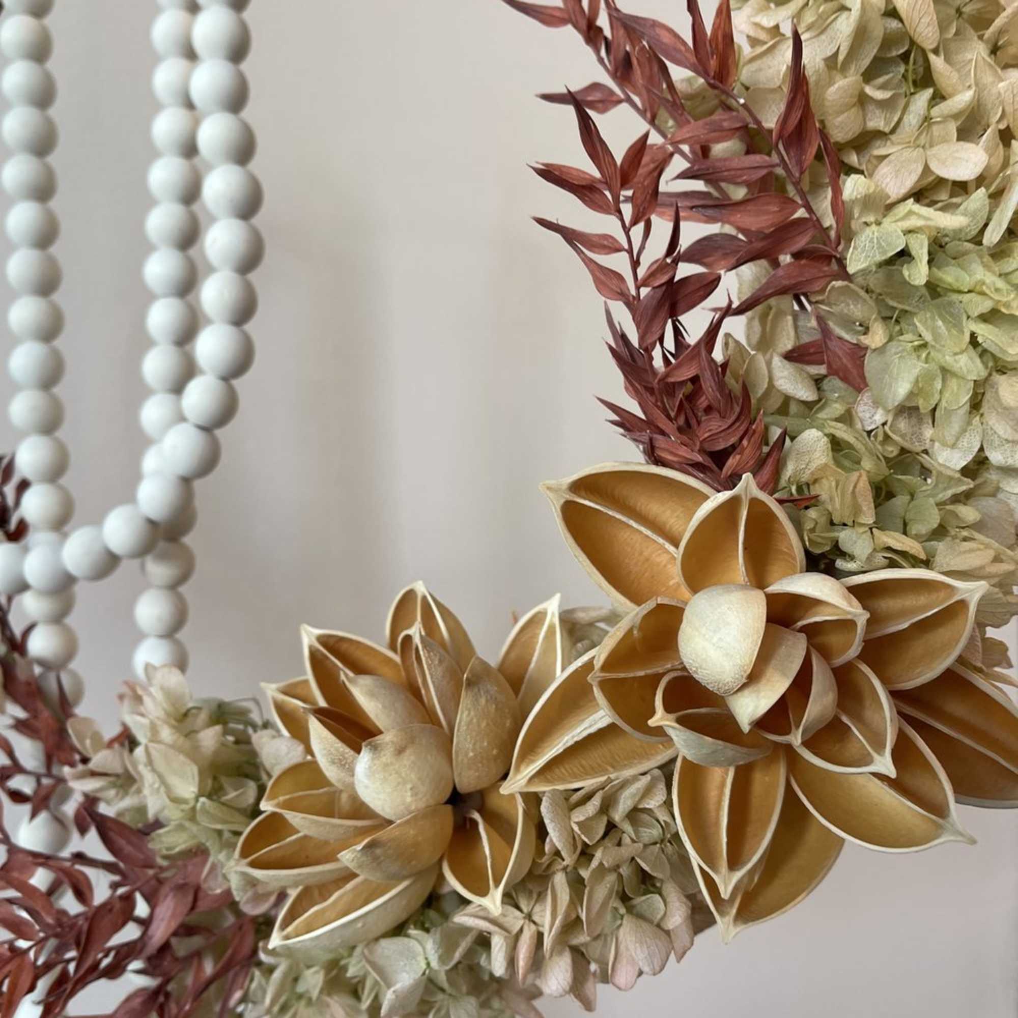 Floral wreath with cream hydrangeas, rust-colored accents, and white bead strands