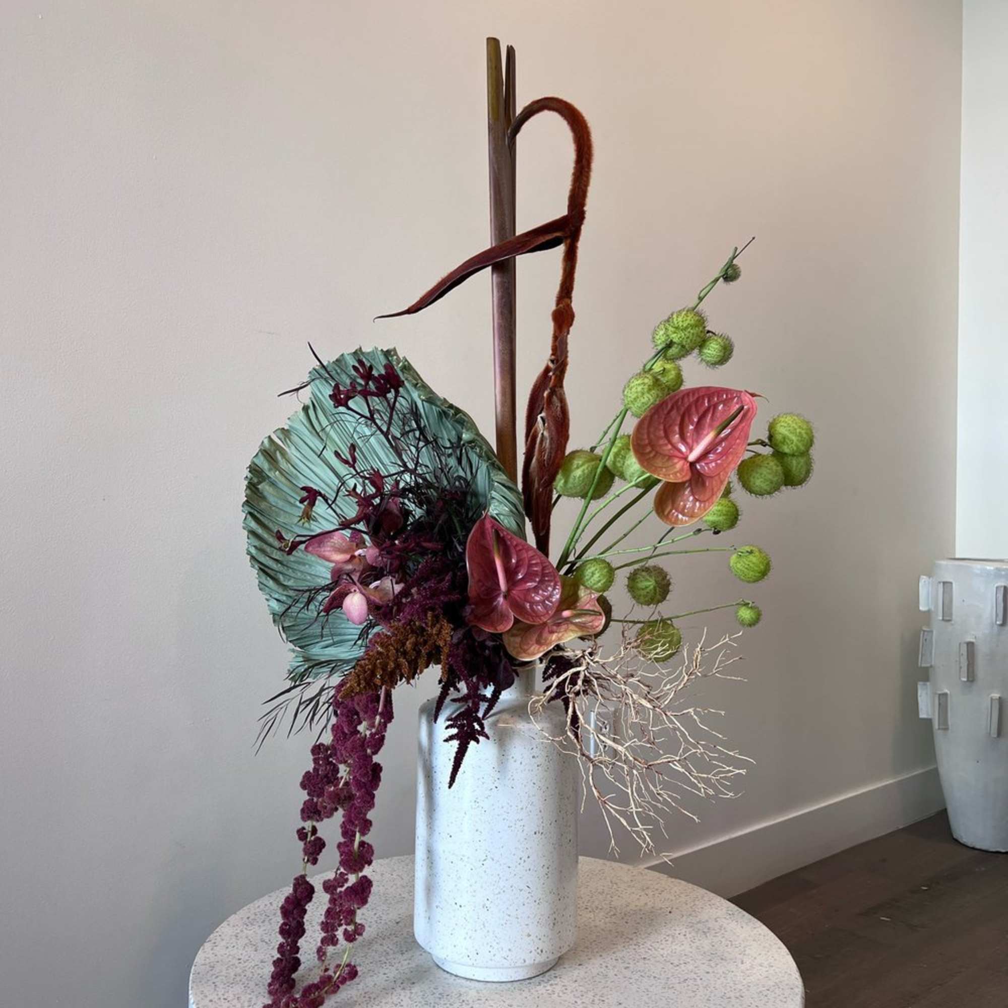 Modern floral arrangement in a white vase with pink anthuriums and green pom-pom stems