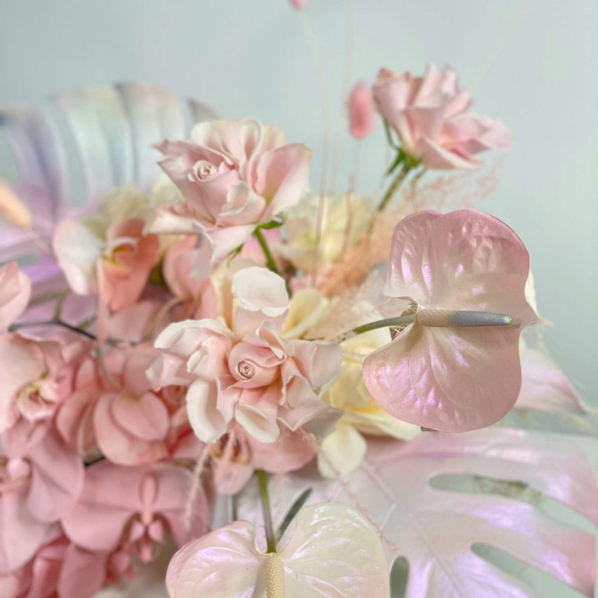 Pastel pink and white flowers arranged with iridescent anthurium blooms
