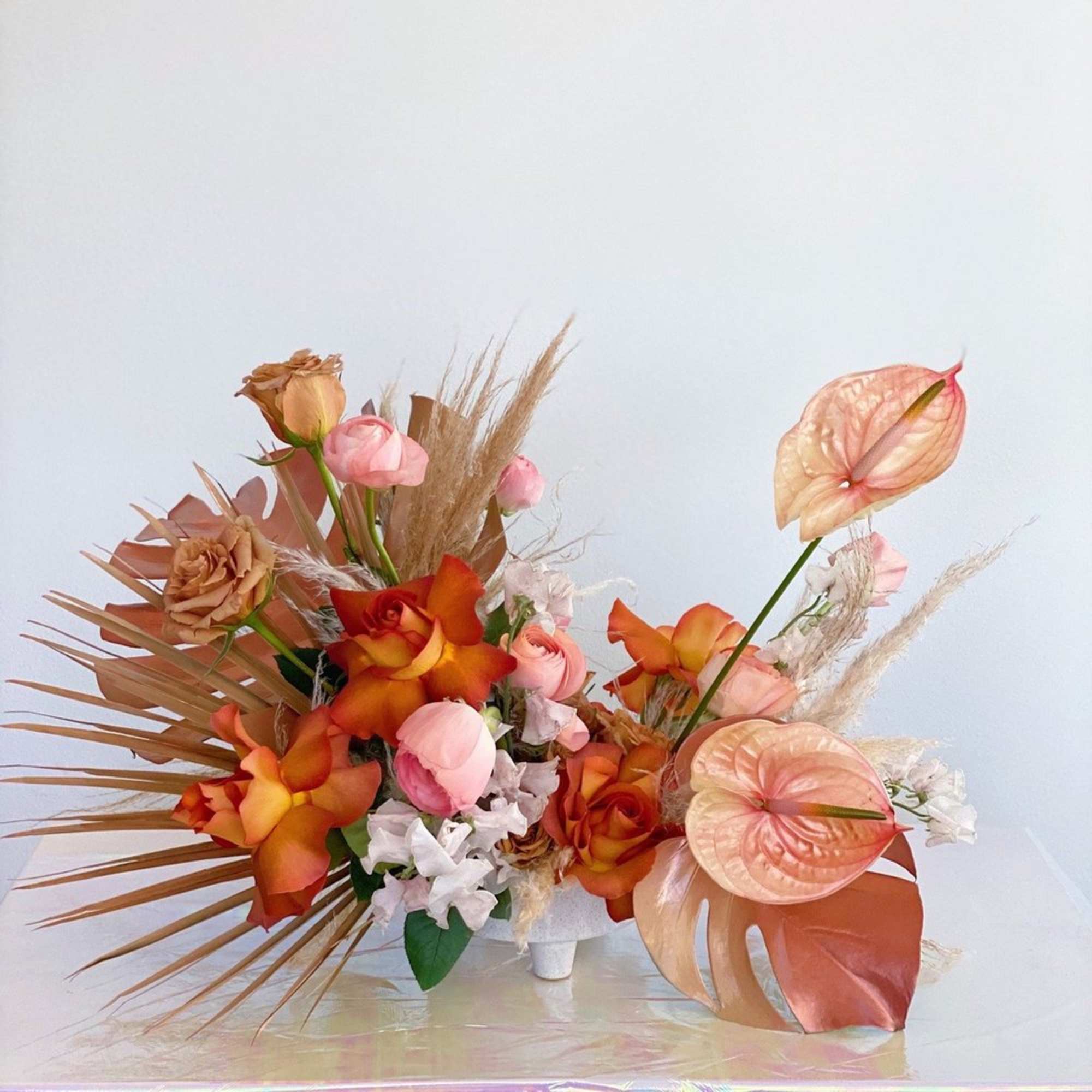 Orange and pink floral arrangement with anthuriums and roses in a white vase