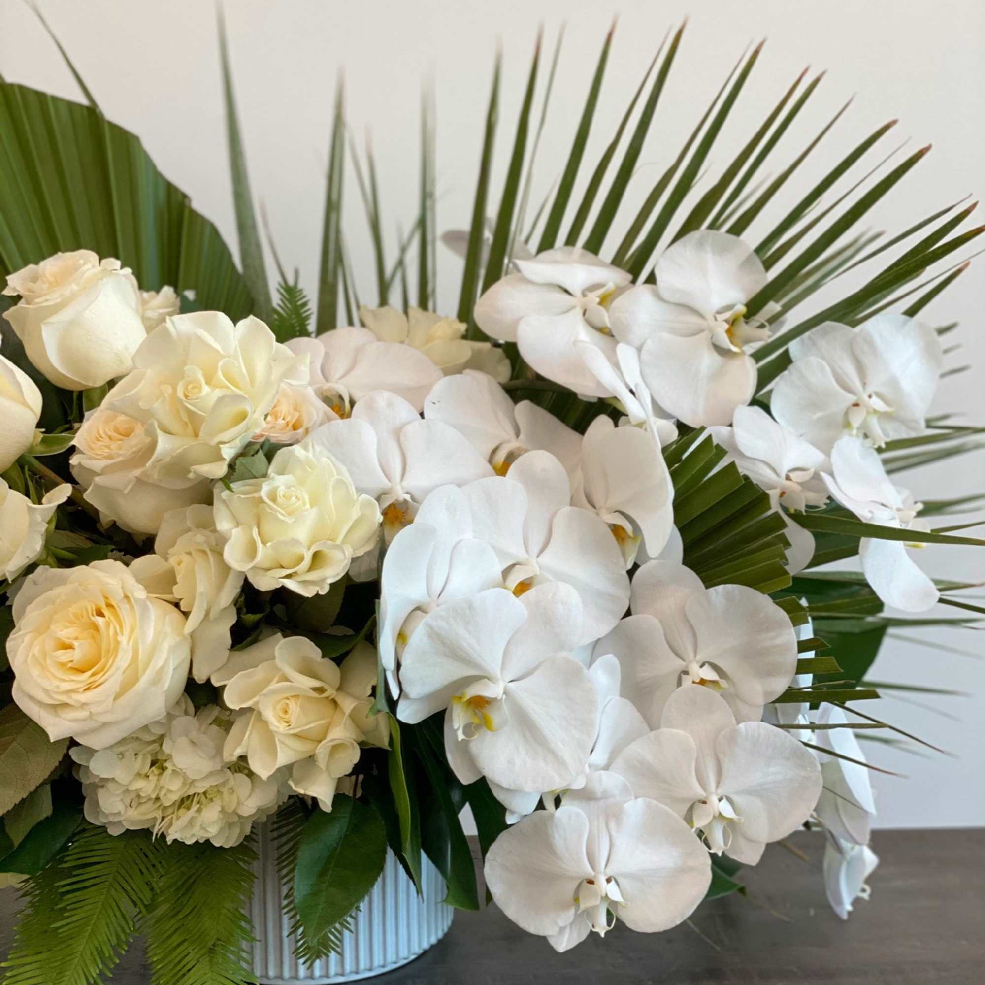 White roses and orchids arranged in a vase with palm fronds