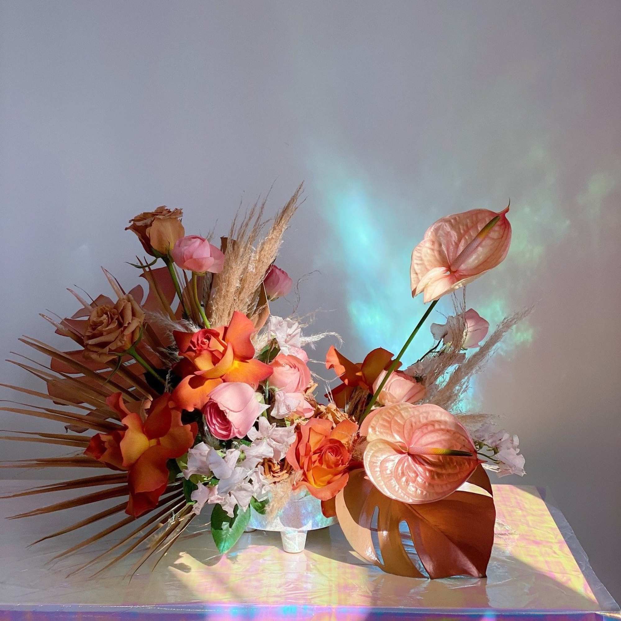 Arrangement of orange and pink flowers with dried grasses in a white vase