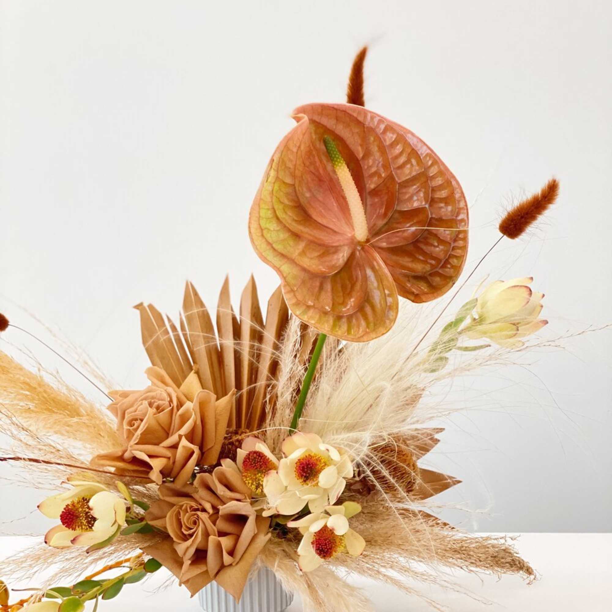 Neutral-toned floral arrangement with anthurium and roses in a ribbed vase