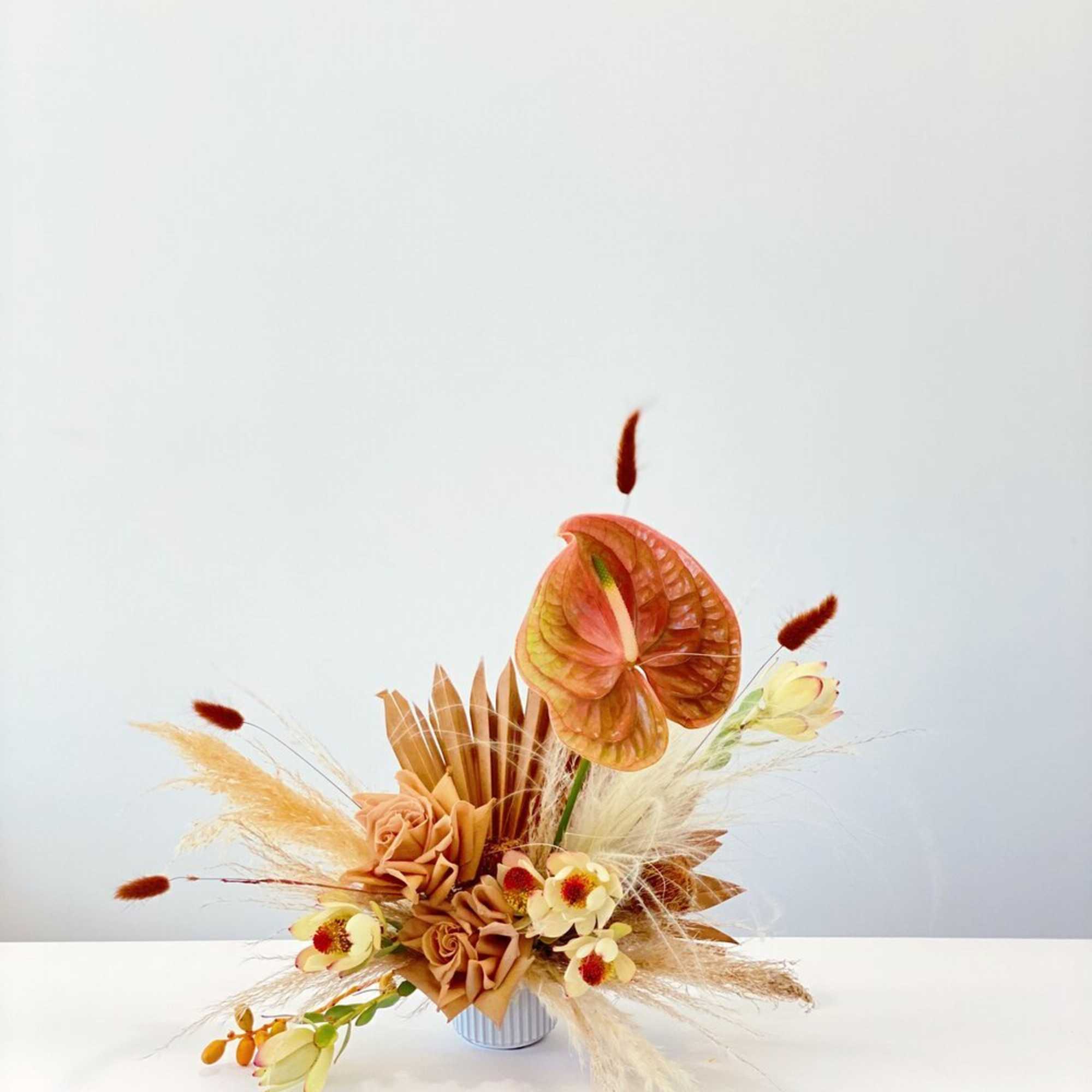 Autumn floral arrangement with peach anthurium and cream flowers in a small vase