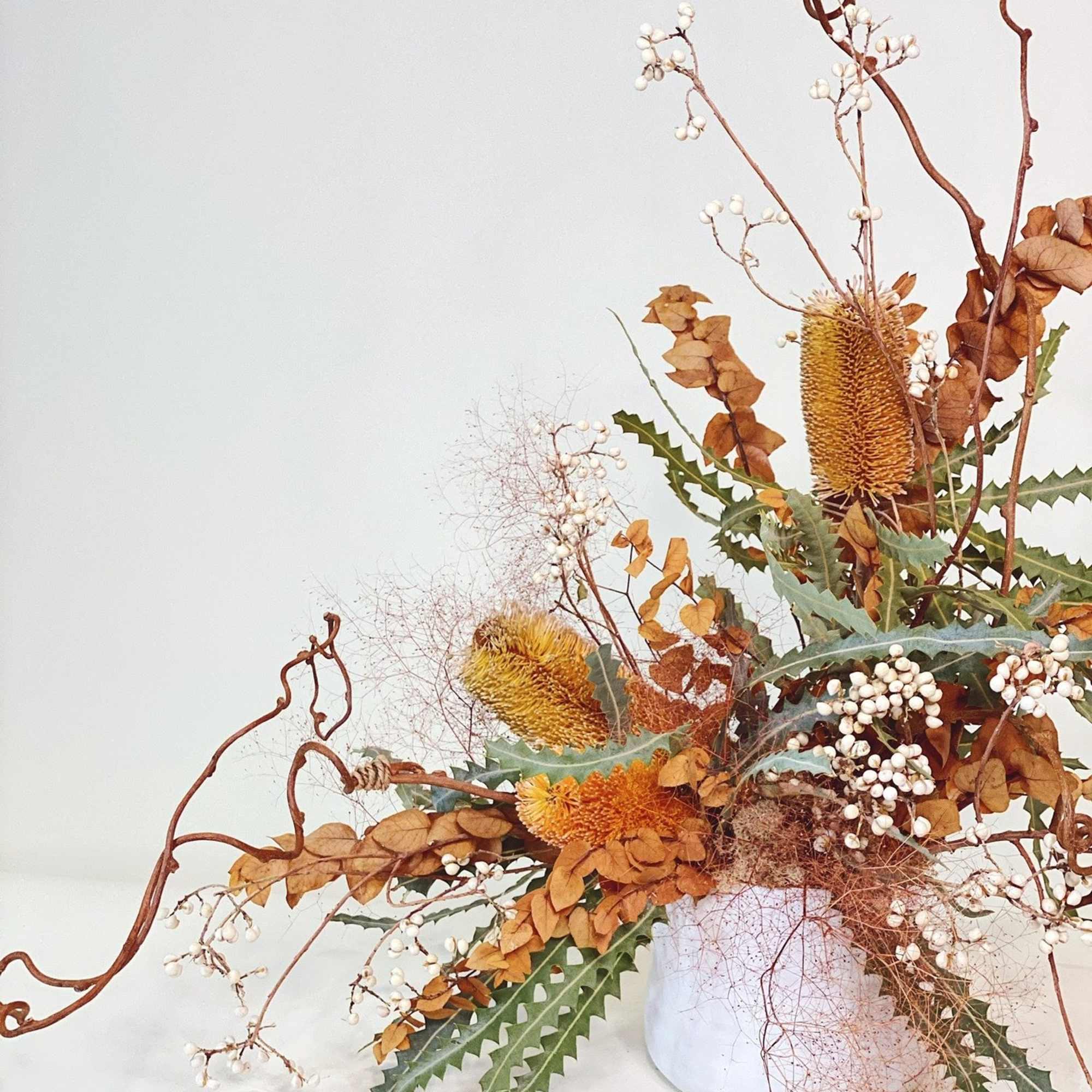 Autumn floral arrangement with orange blooms and white berries in a white vase