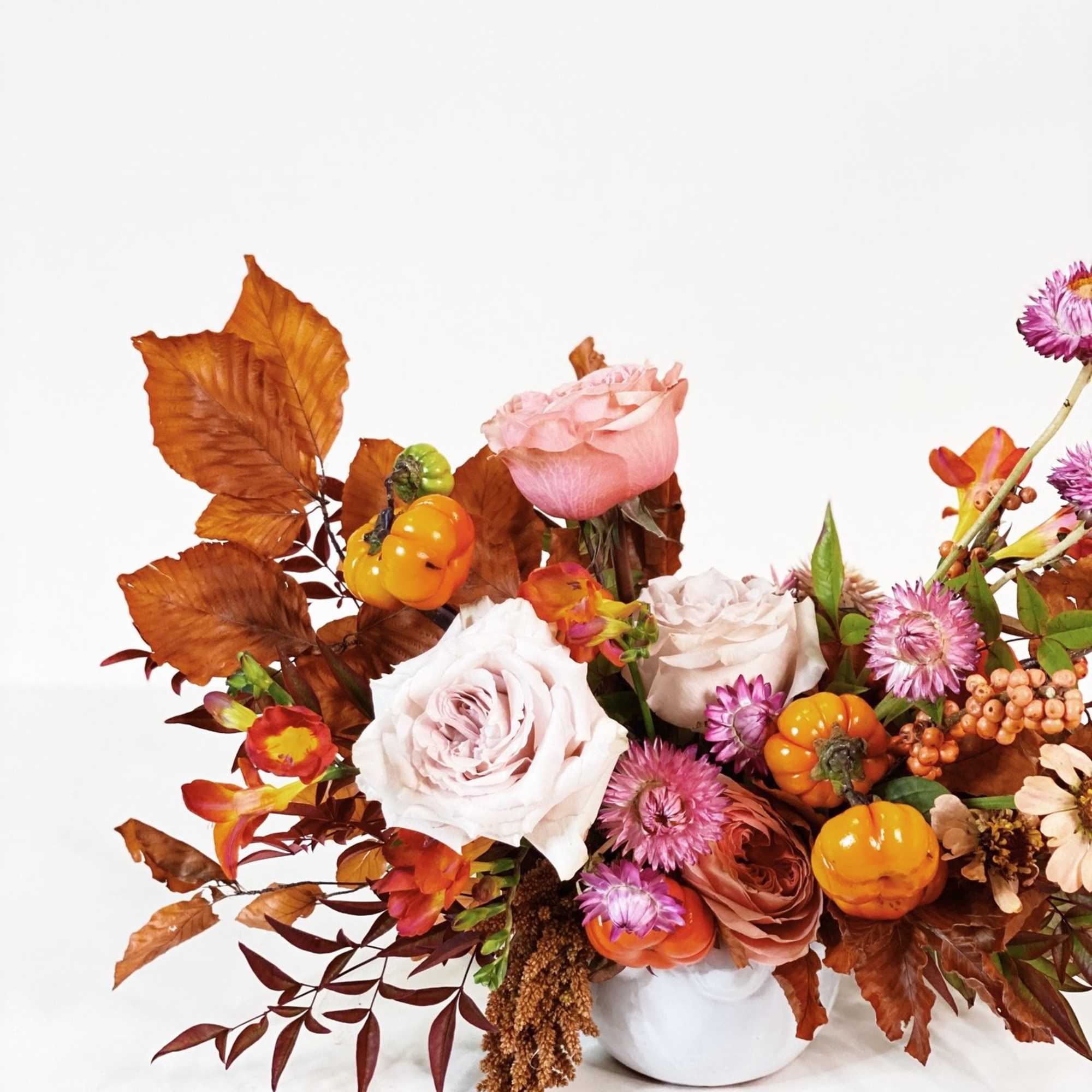 Autumn floral arrangement with pale roses and orange pumpkins in a white vase