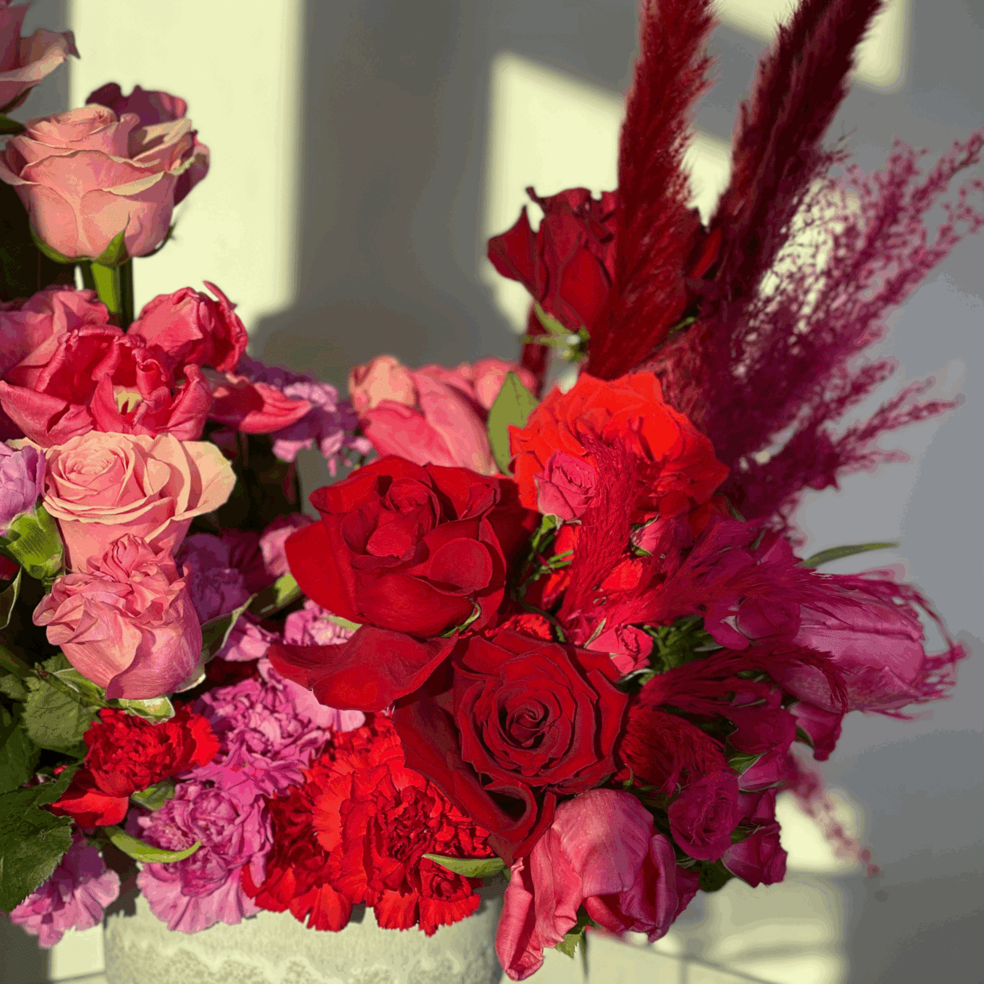 Red and pink rose arrangement in a textured white vase