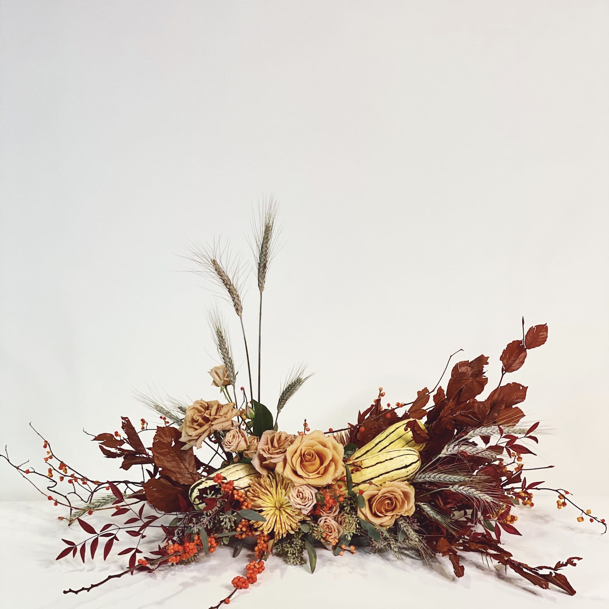 Low floral arrangement with peach roses, wheat stalks, and autumn leaves