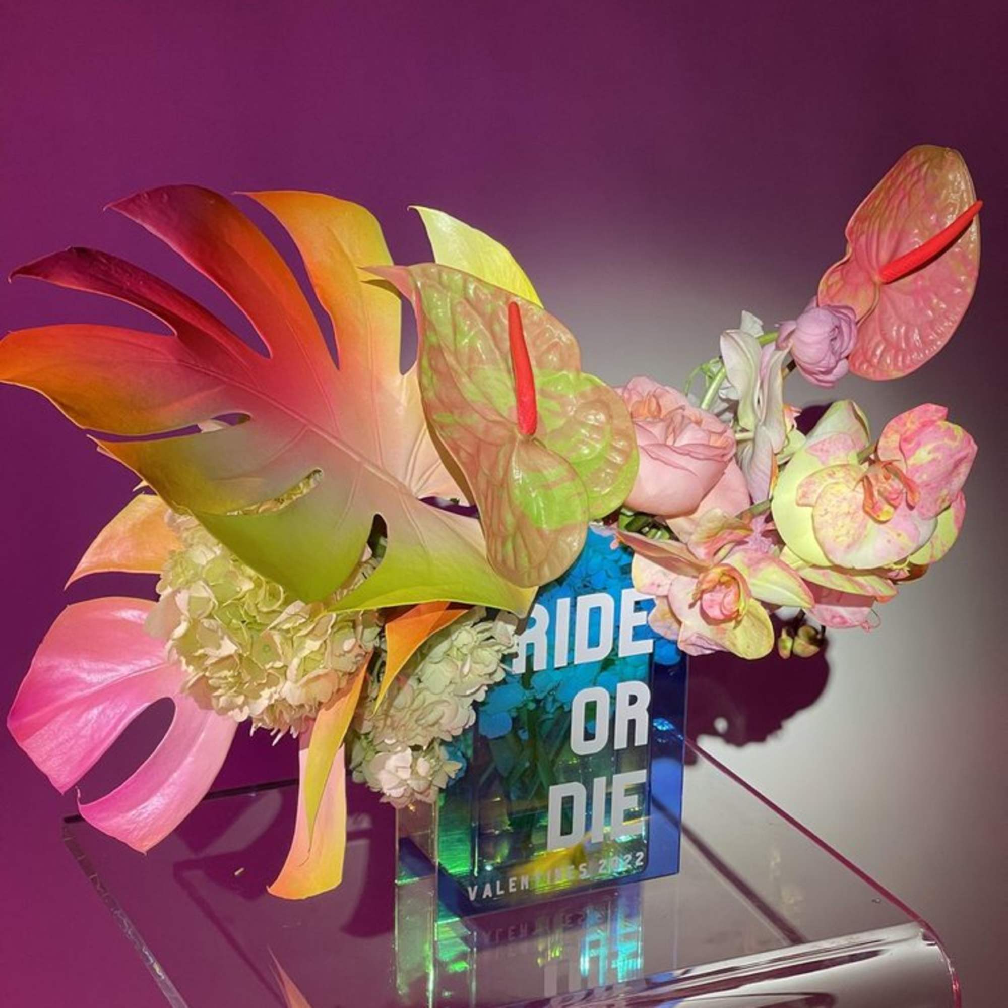 Tropical floral arrangement with anthuriums and monstera leaves in a clear acrylic vase