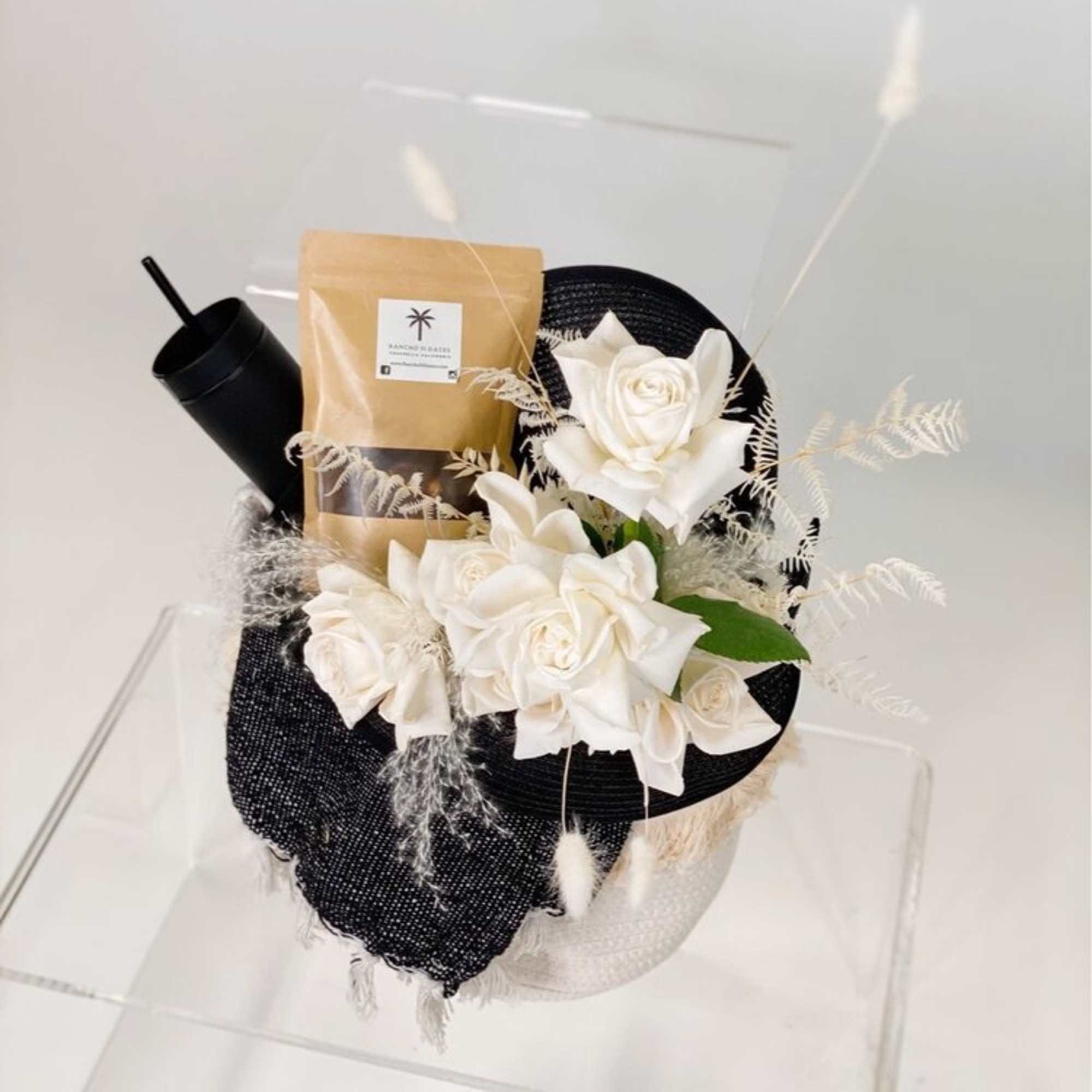White roses arranged with a black tumbler and packaged gift bag