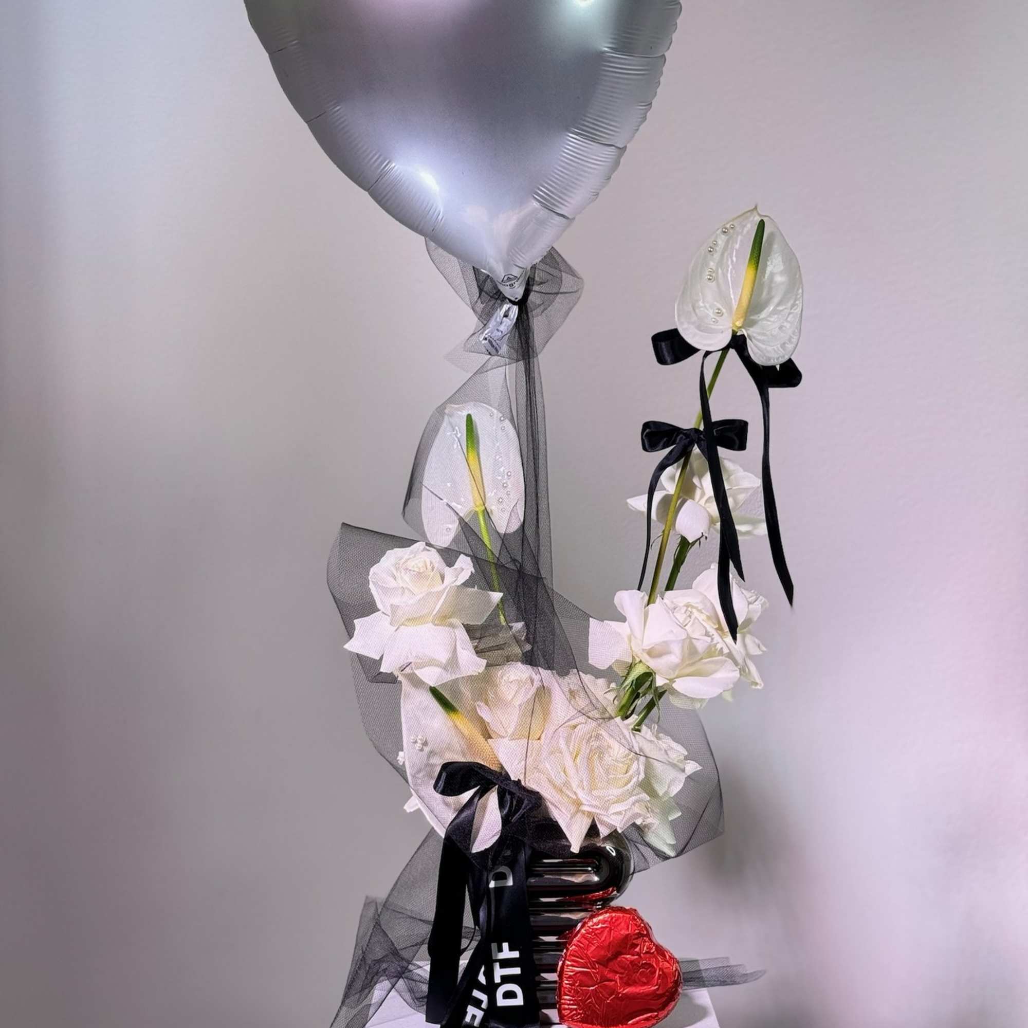 White roses and anthuriums with a silver heart balloon and red heart candy