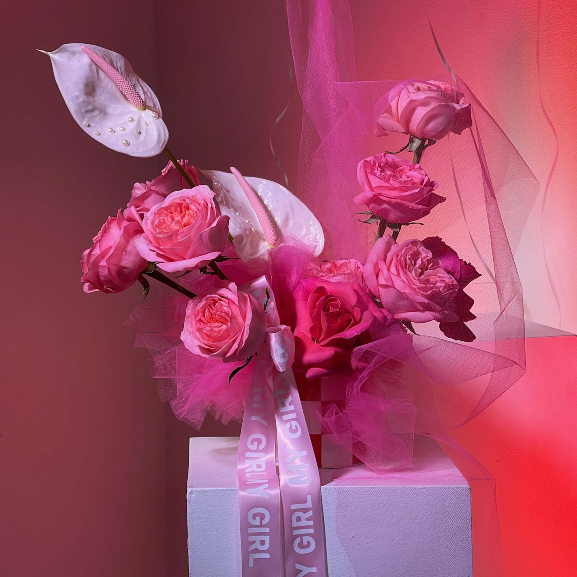 Pink rose arrangement with white anthuriums and a ribbon on a pedestal