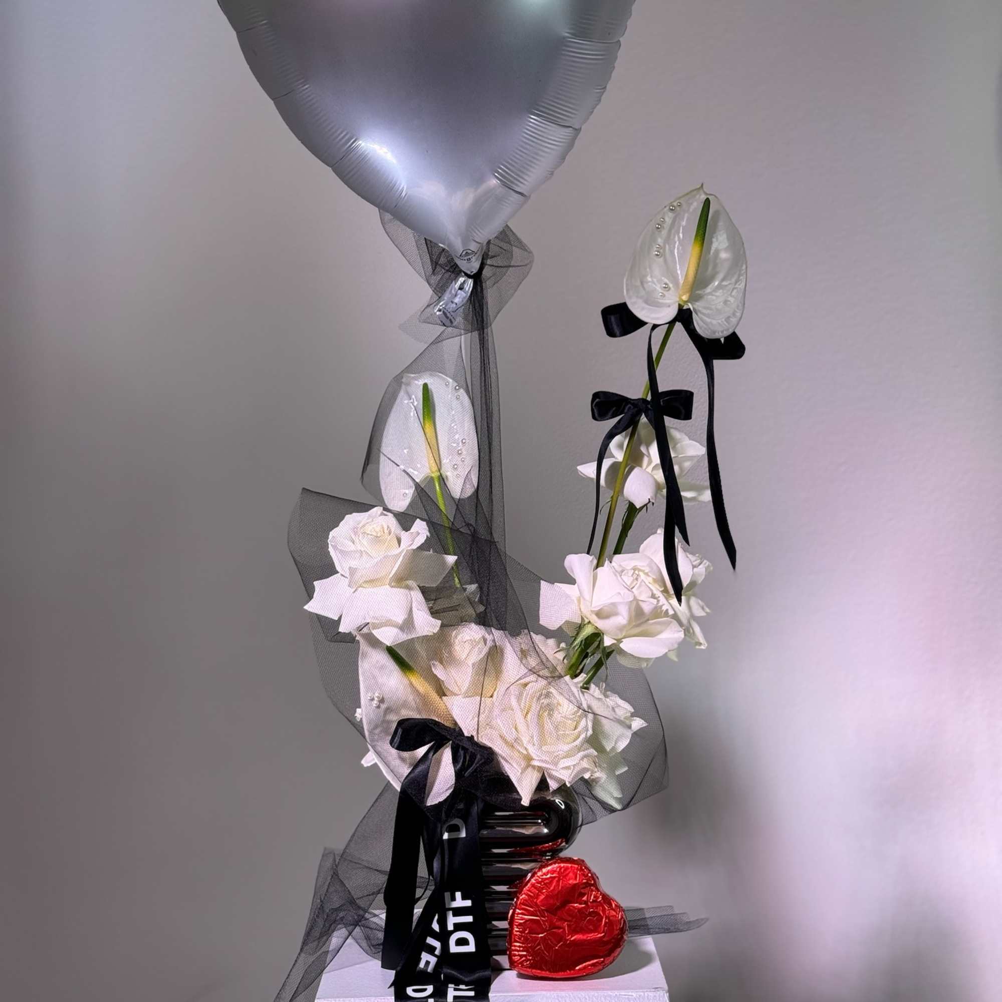 White roses with an anthurium and silver heart balloon on a pedestal