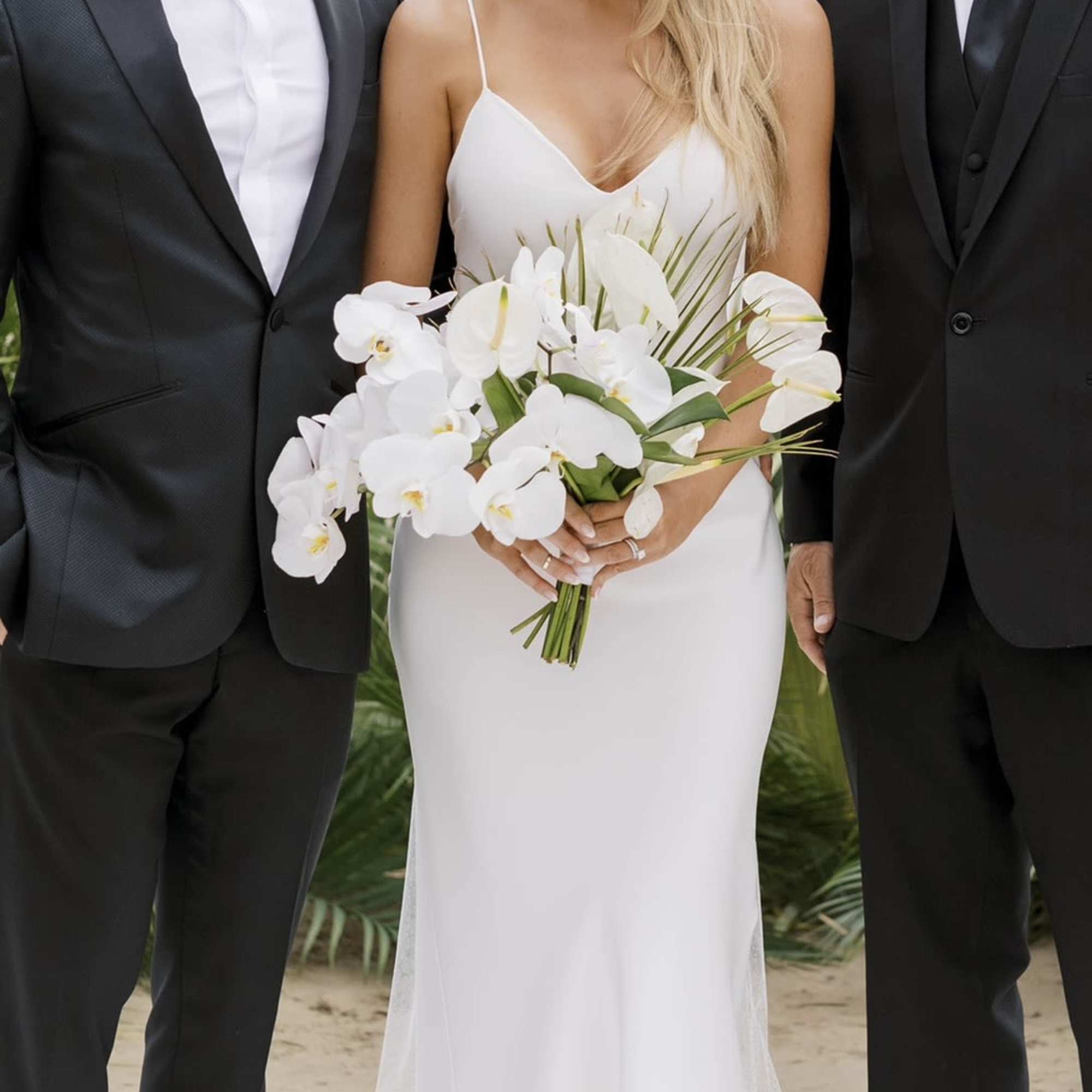 Bride holding a white orchid bouquet beside two men in black suits
