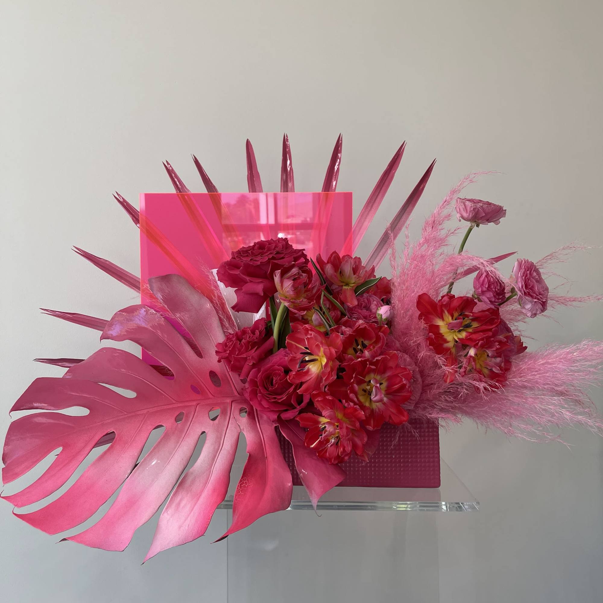 Pink floral arrangement with tropical leaves and a clear vase
