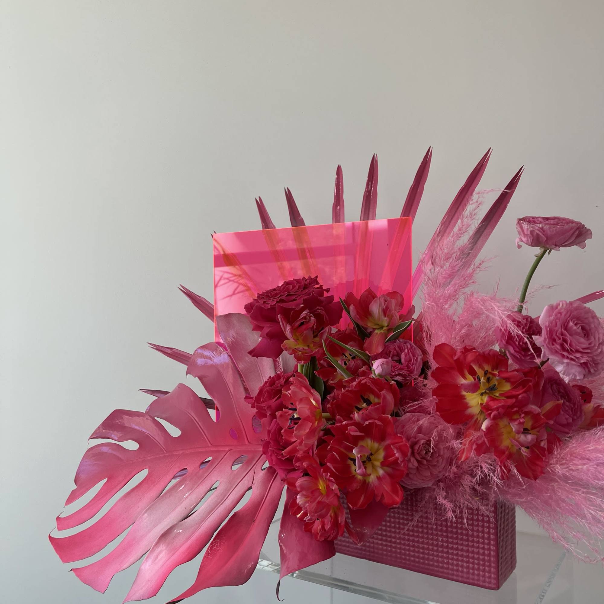 Bright pink floral arrangement with tropical leaves in a pink box