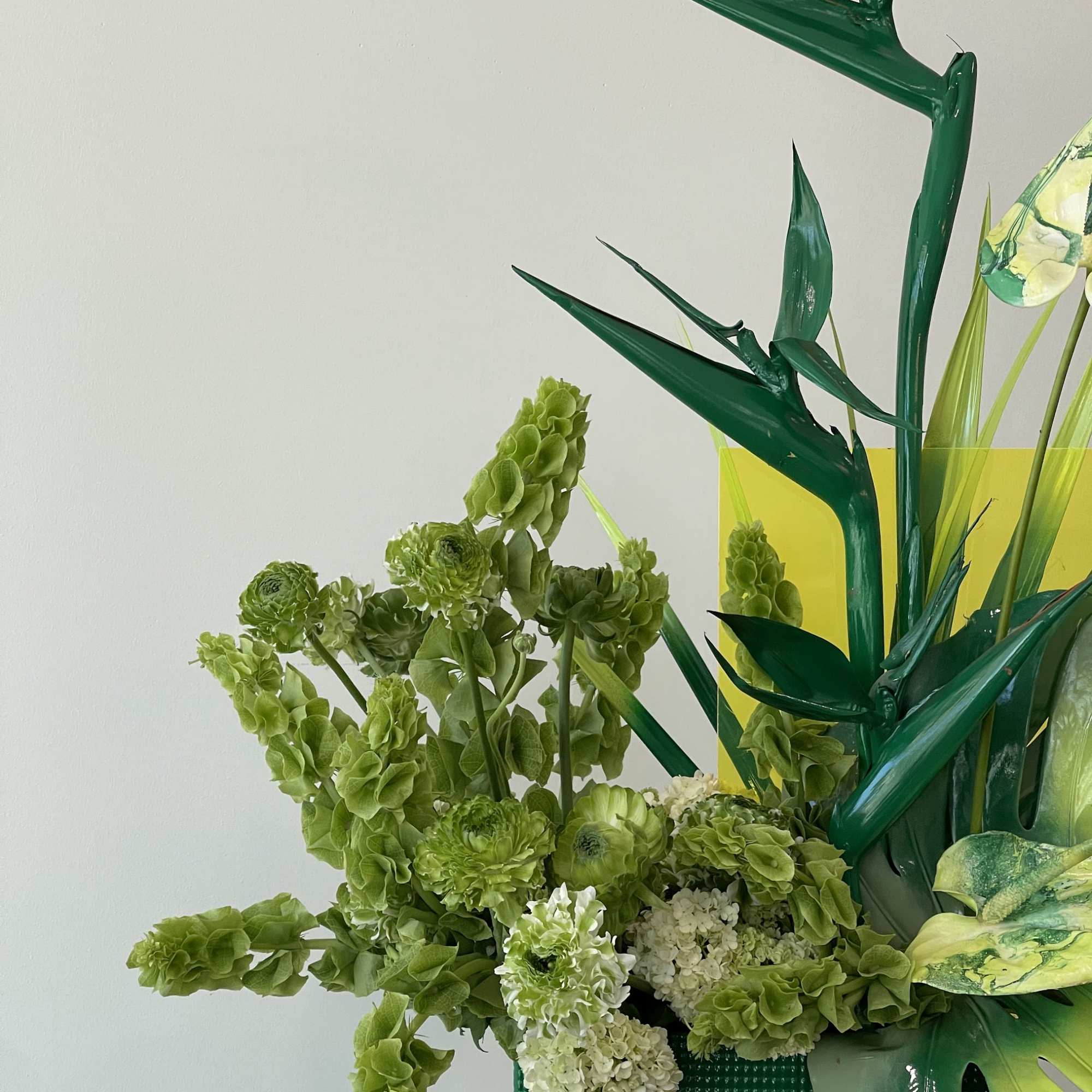 Green floral arrangement with tall tropical leaves and clustered blooms in a green container