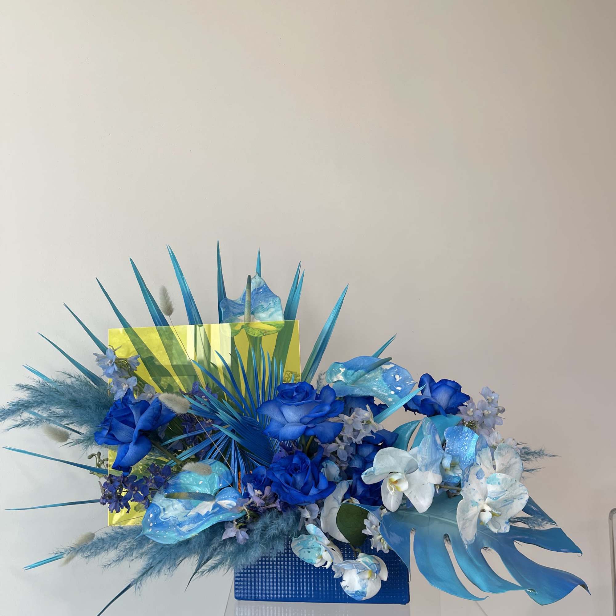 Blue floral arrangement with orchids and roses in a rectangular vase