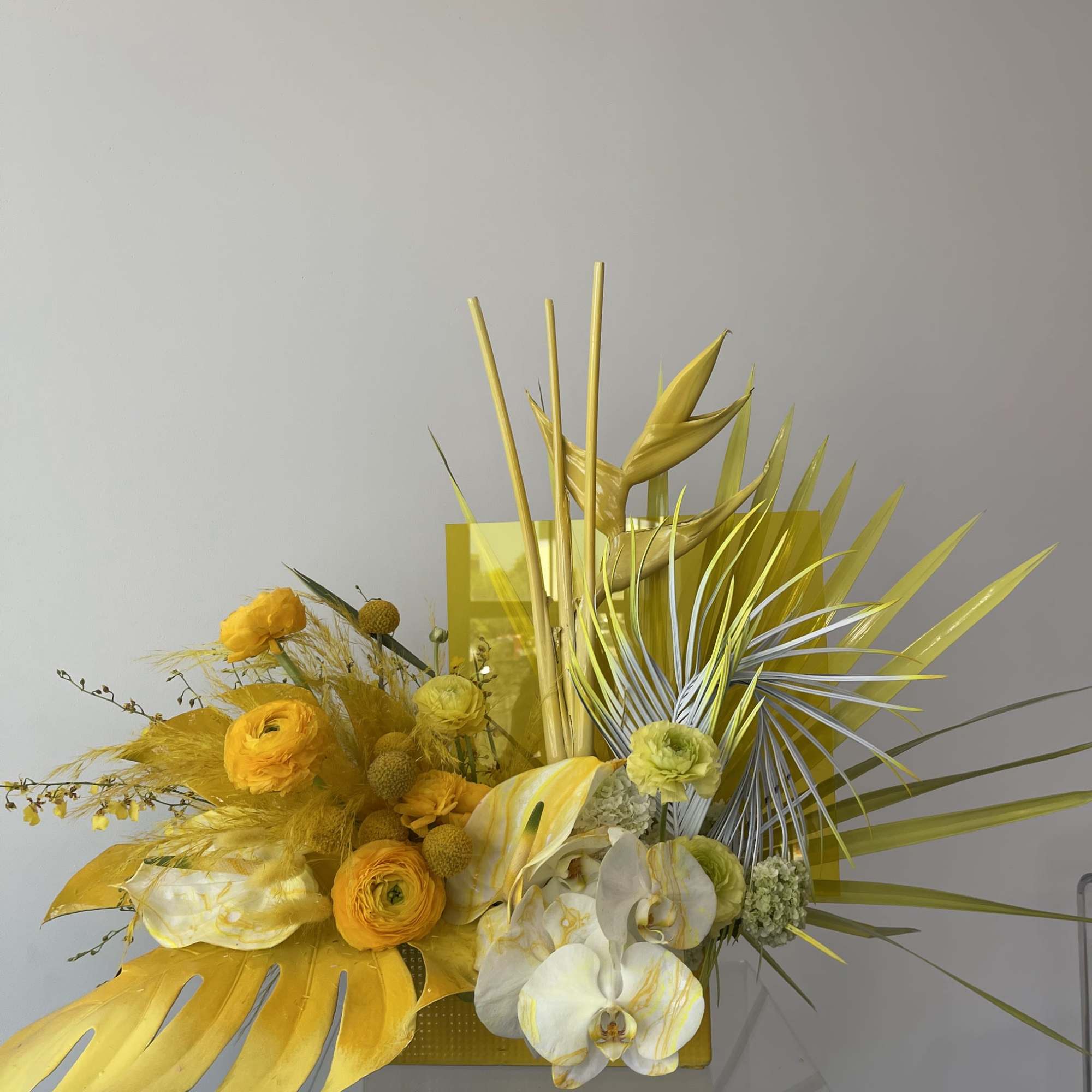Yellow floral arrangement with orchids and tropical leaves in a rectangular container