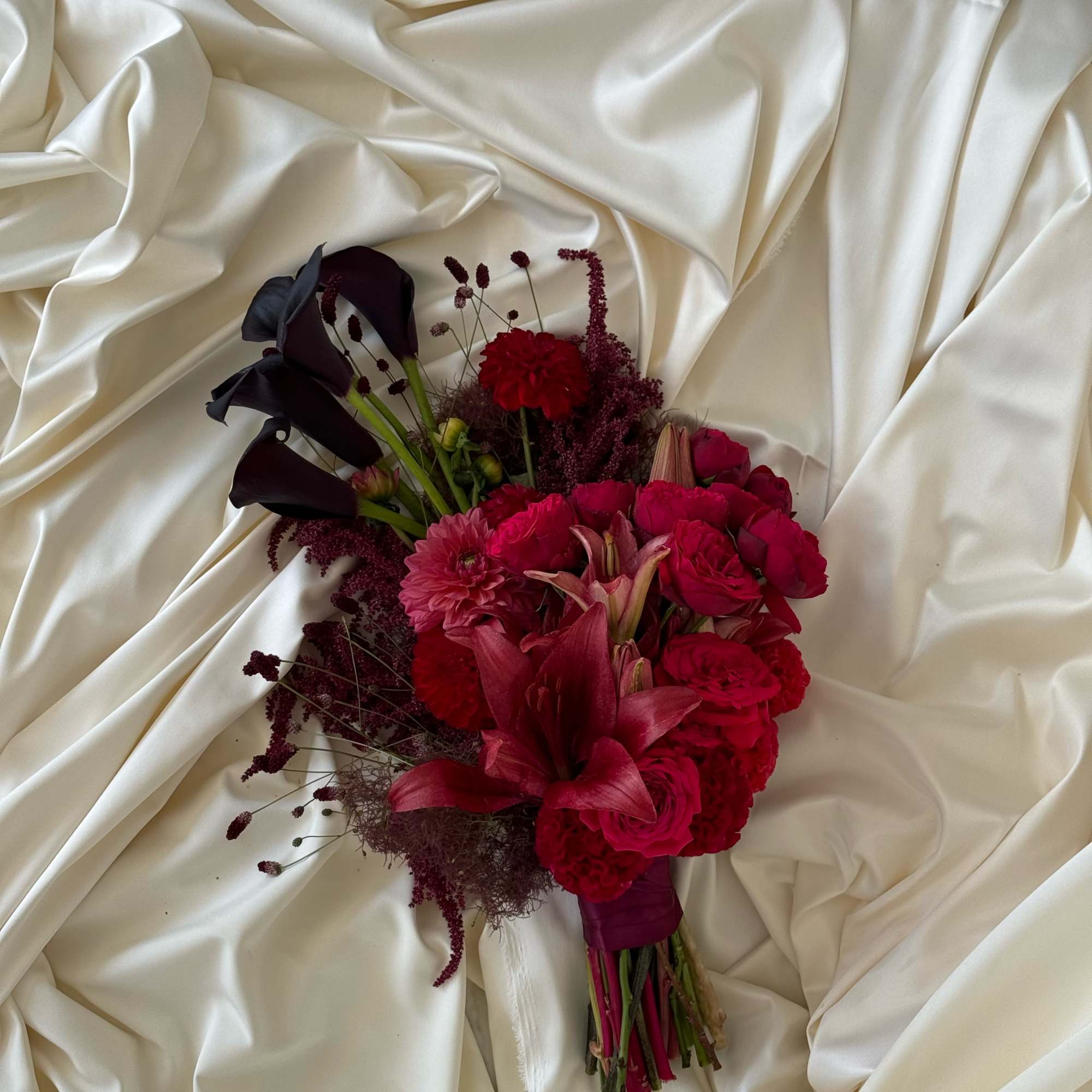 Bouquet of deep red and dark purple flowers on cream satin fabric