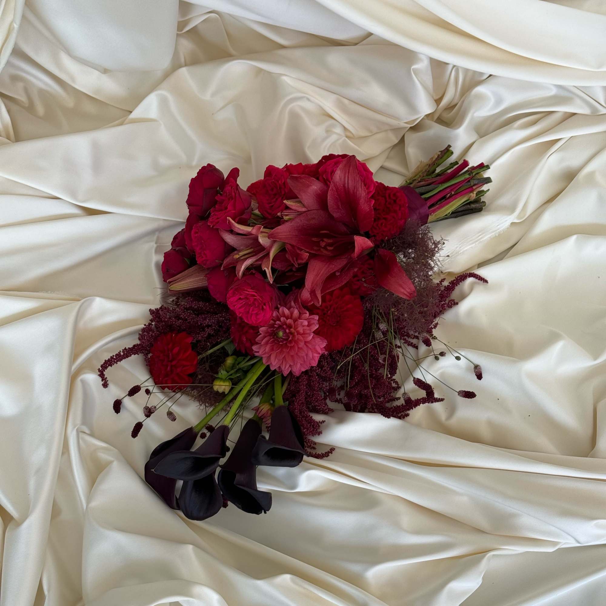 Deep red bouquet with lilies, roses, and dark calla lilies on ivory satin