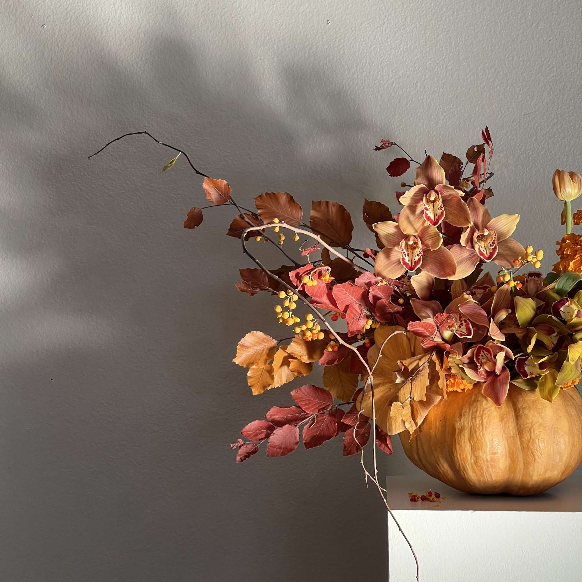 Autumn floral arrangement in a pumpkin vase with orchids and orange leaves