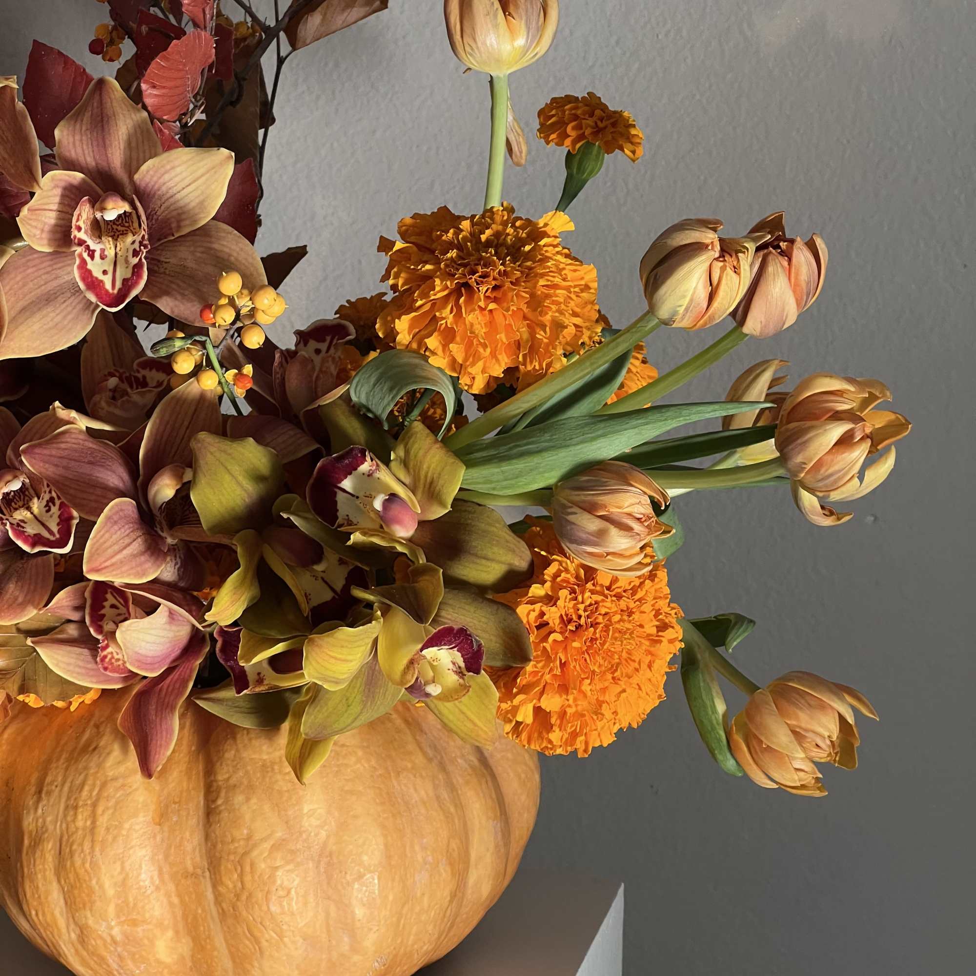 Orange pumpkin vase with orchids, tulips, and marigolds