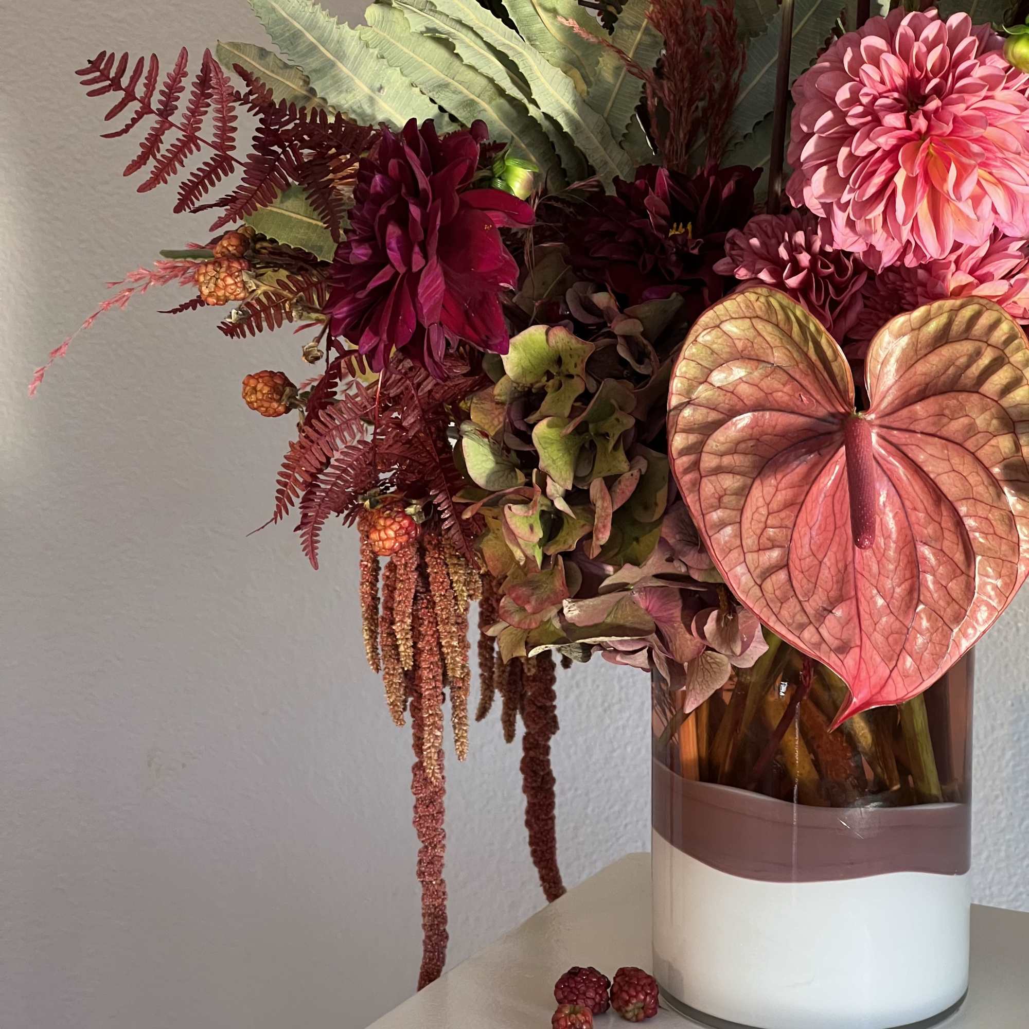 Pink and burgundy floral arrangement in a glass vase with anthurium and dahlias