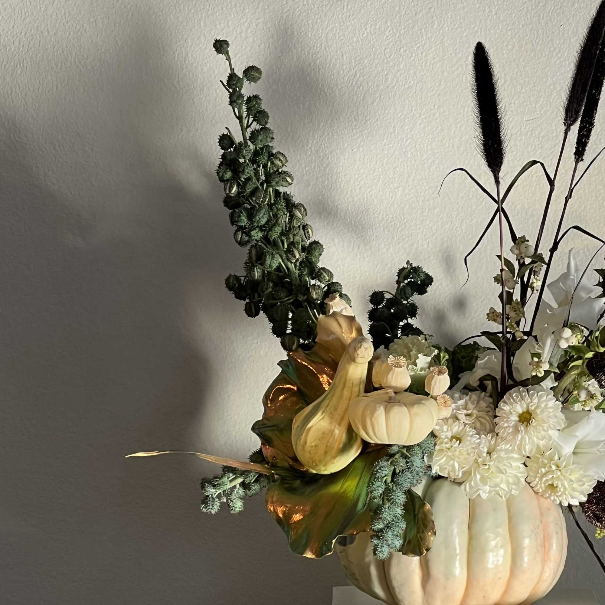 White flowers arranged in a pumpkin-shaped container with dried seed pods
