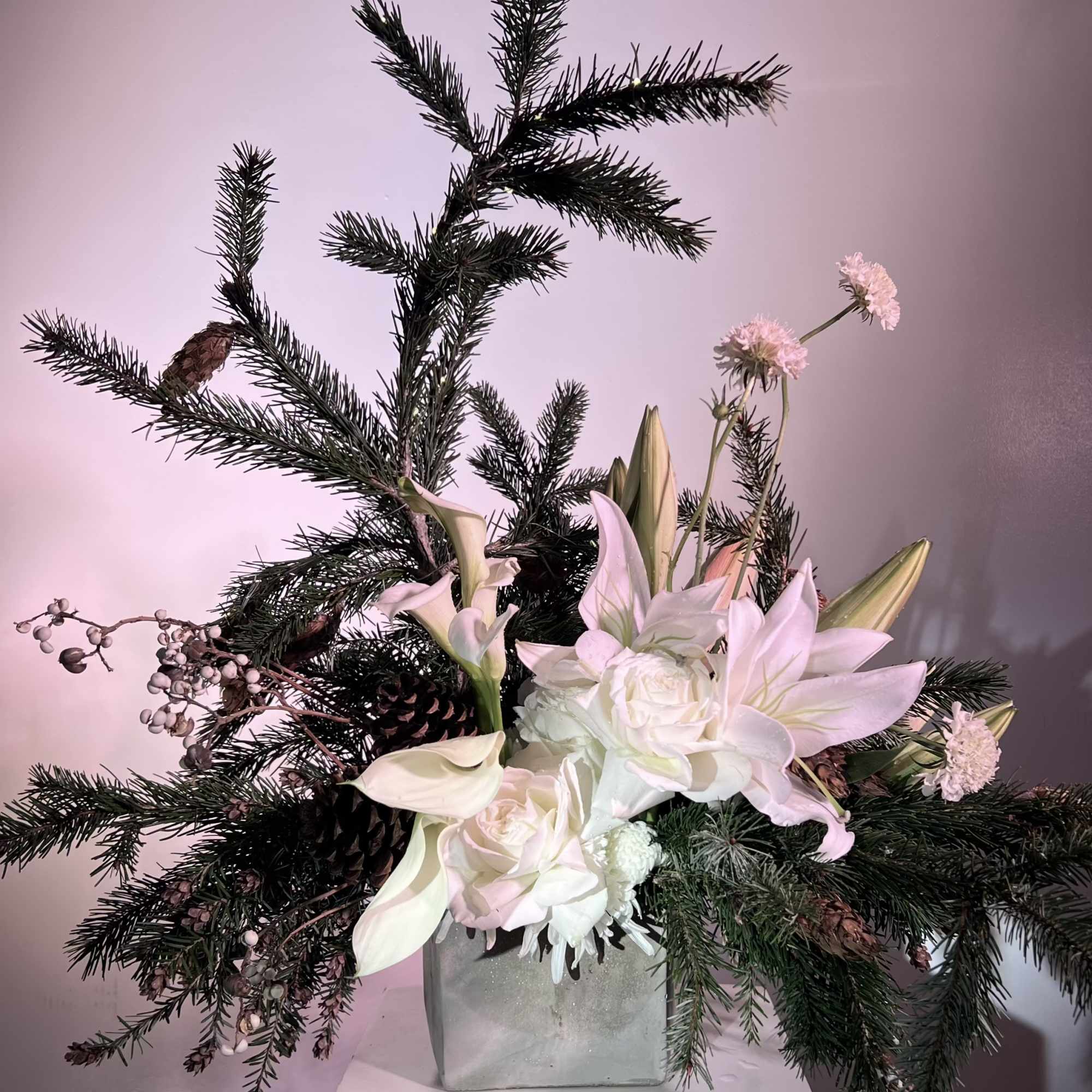 White lilies and roses arranged with pine branches in a square vase