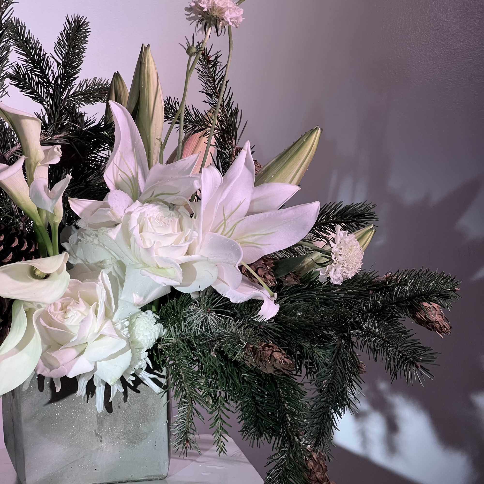 White lilies and roses arranged with evergreen branches in a square vase