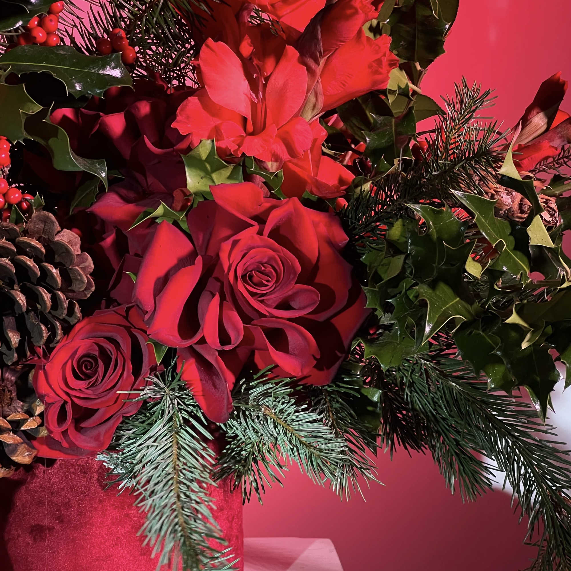 Red roses and red flowers in a glittery vase with pinecones and evergreen branches
