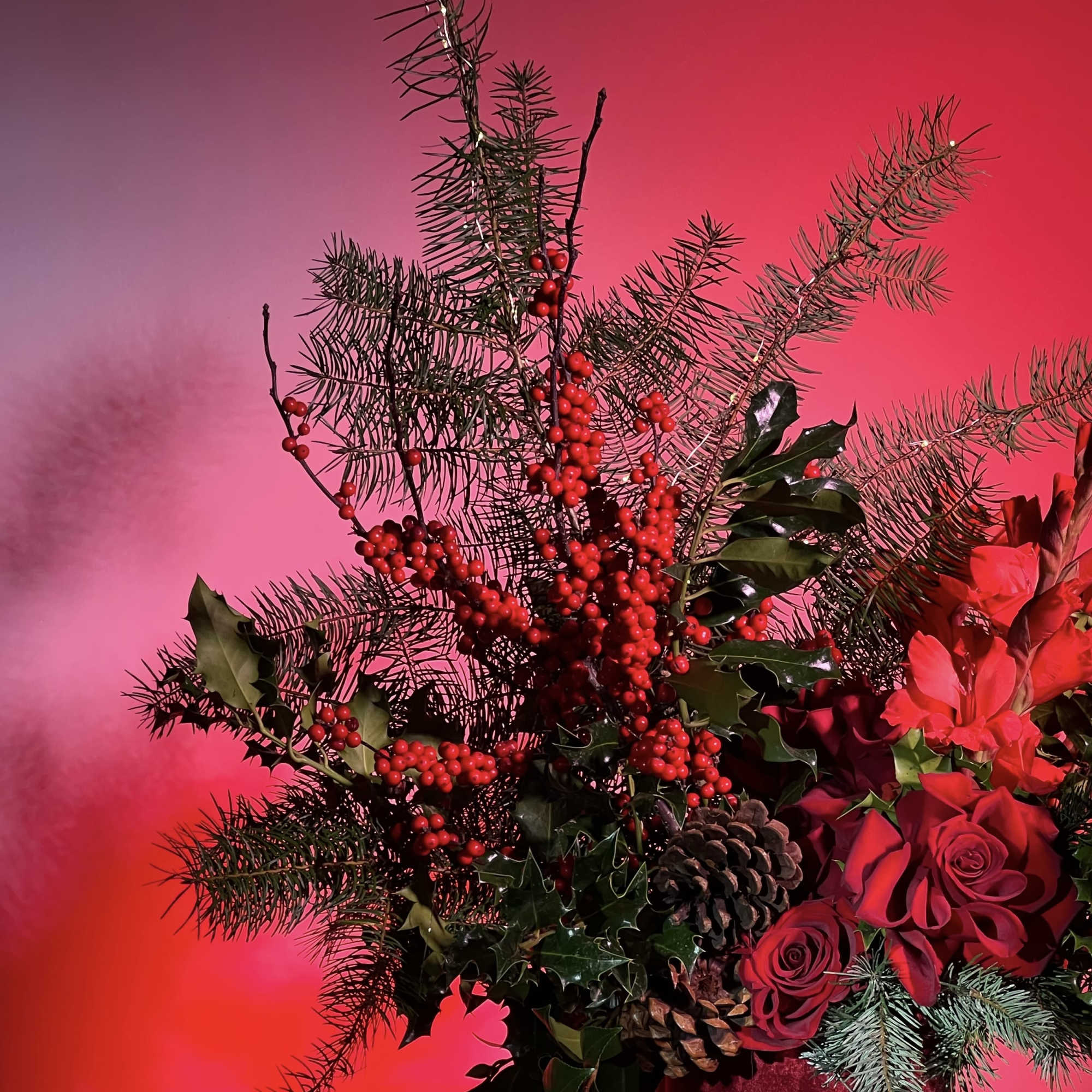 Red floral arrangement with berries, pine branches, and roses in a vase