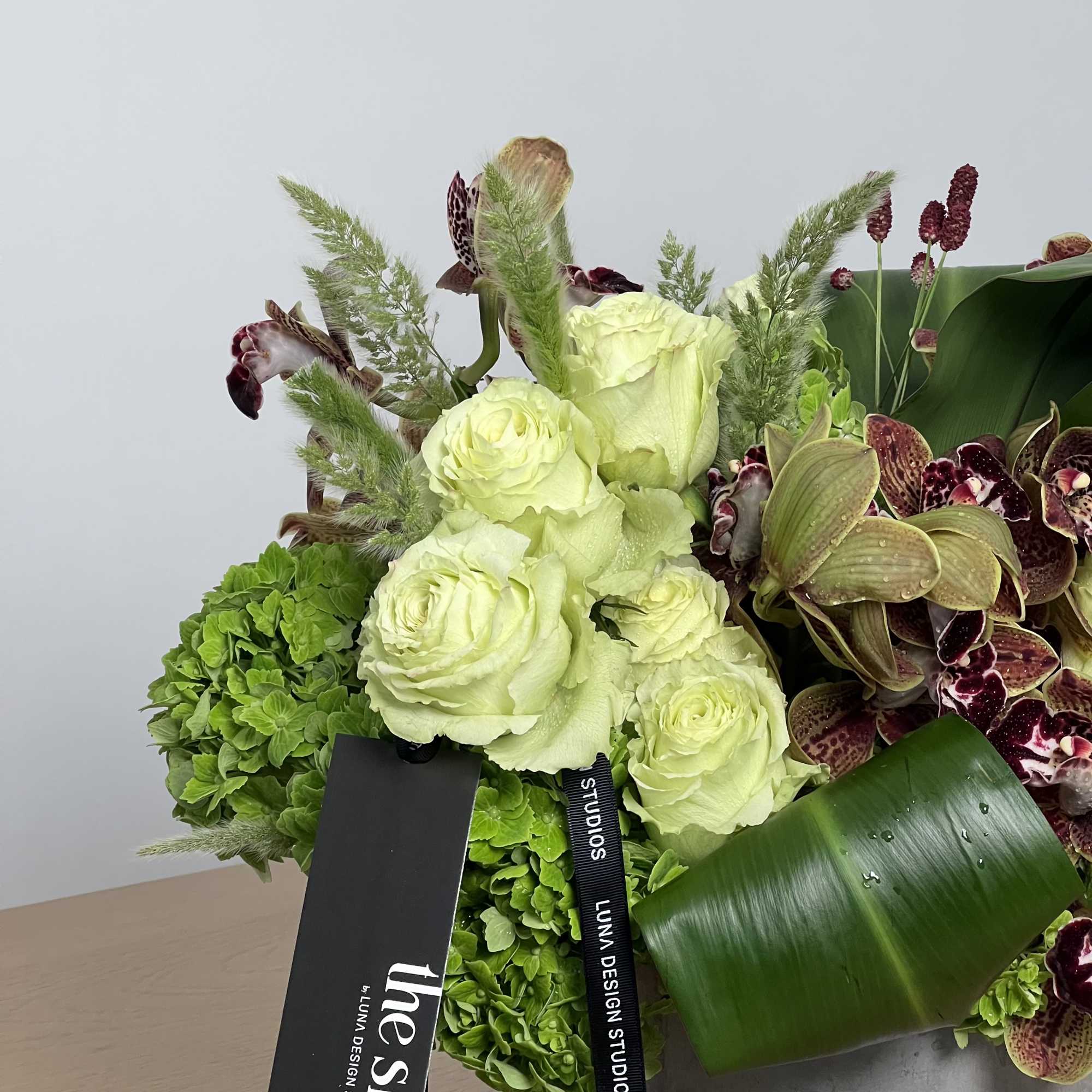 Arrangement of pale green roses and orchids in a gray vase