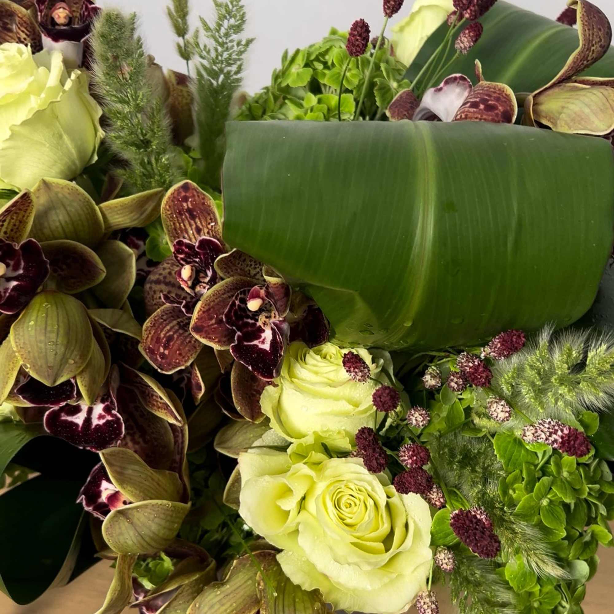 Bouquet of pale yellow roses and dark orchids with green foliage